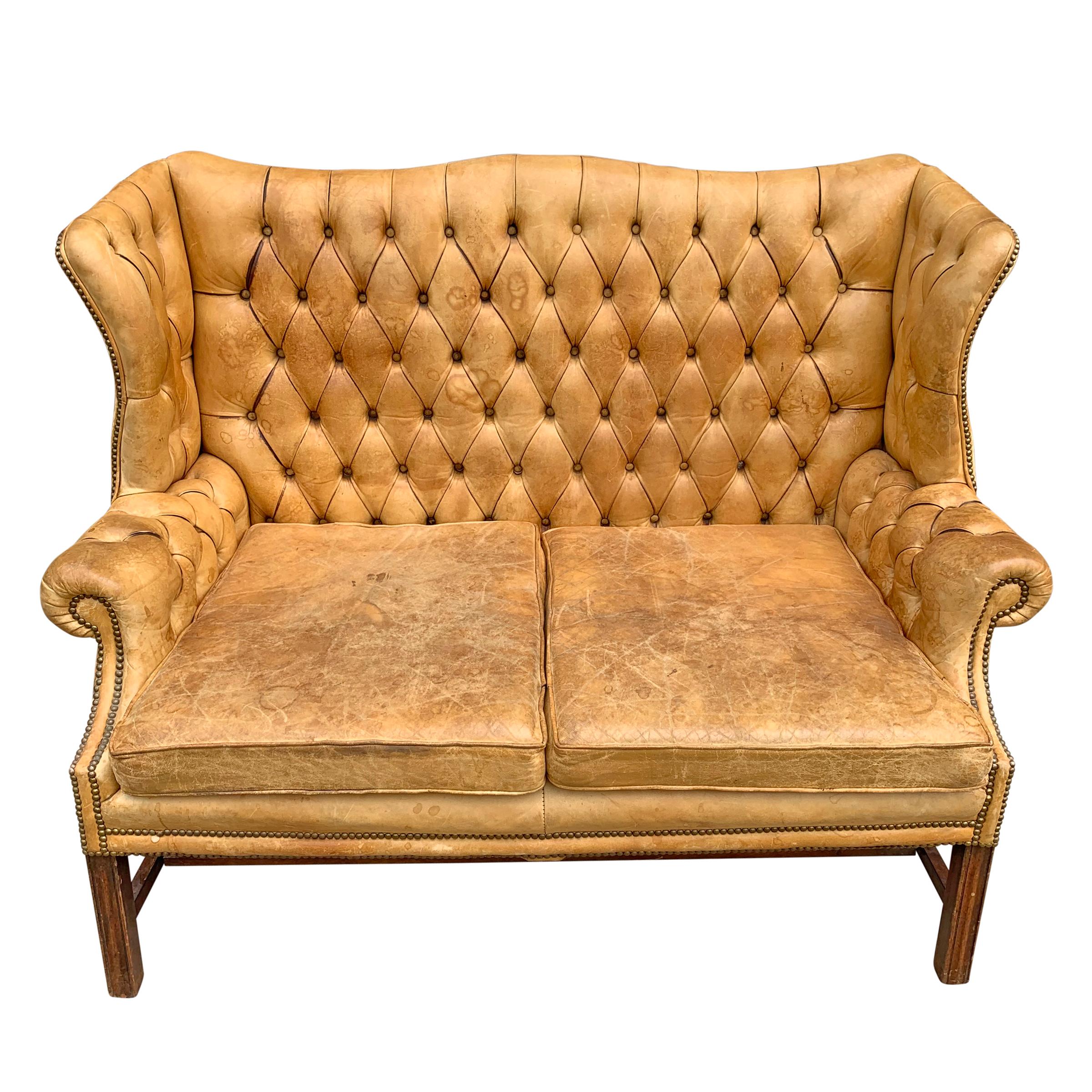 A fantastic early to mid-20th century English Chippendale-style tufted leather wingback settee with a wonderful form, super comfortable seat, and brass nailhead trim.