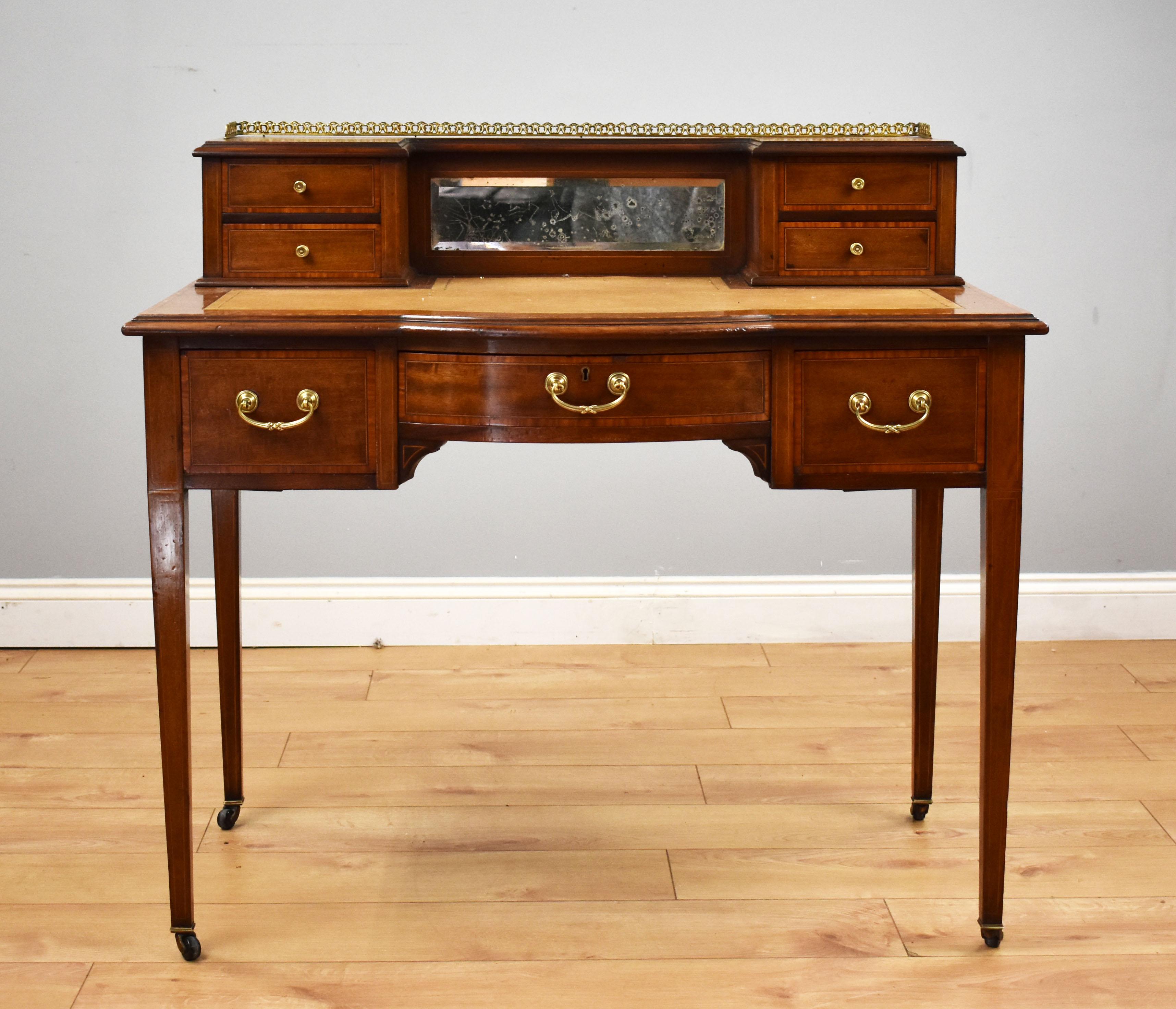 For sale is an Edwardian mahogany writing table, with a rear upstand with drawers and a mirror, tooled leather writing surface and a satinwood banded edge, having three frieze drawers below. The desk stands on elegant tapered legs terminating on
