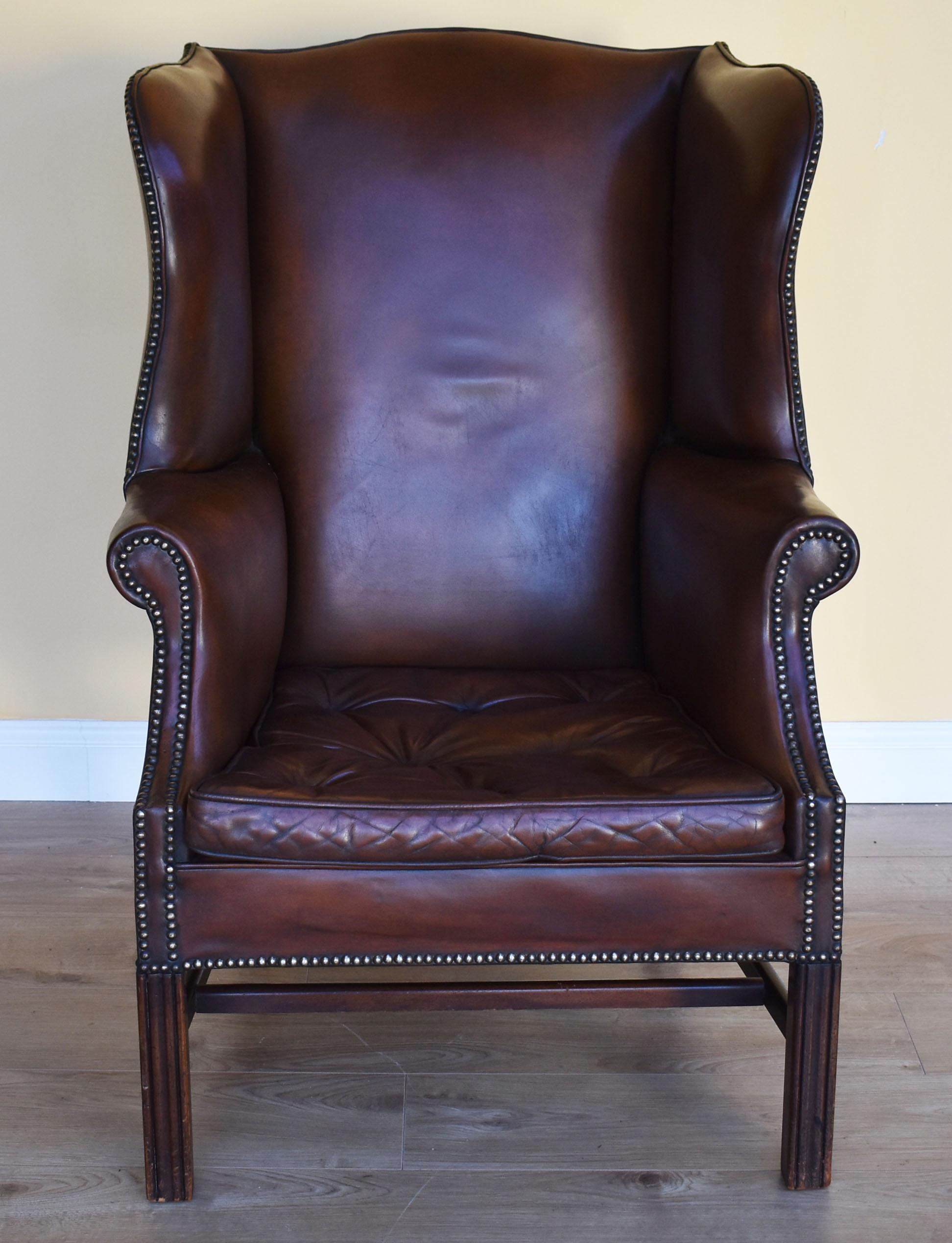 For sale is a good quality Georgian style mahogany and leather wingback armchair, upholstered in hand dyed brown leather, standing on square legs united by a central stretcher. The chair has a removable seat with 