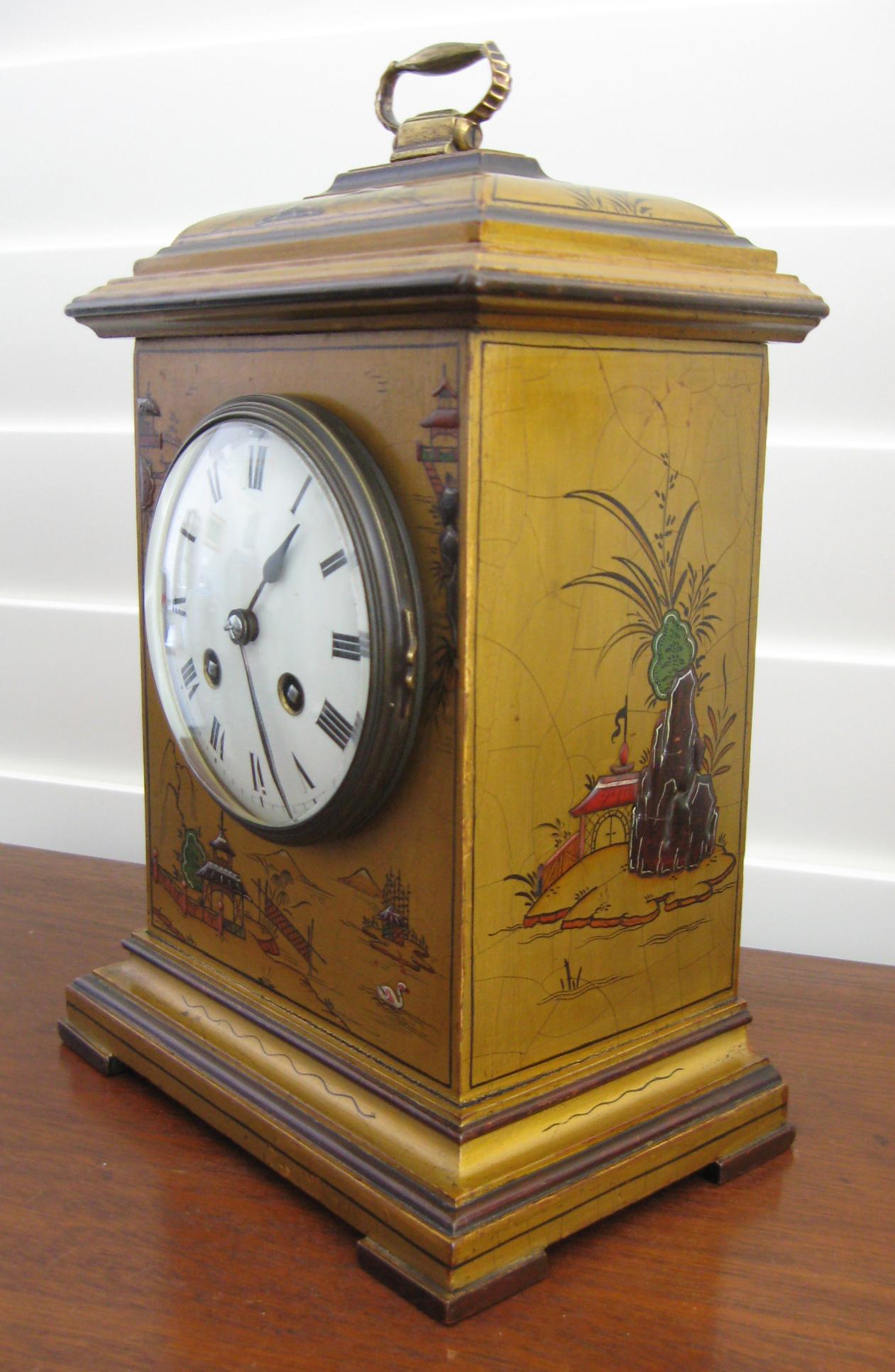 A decorative two train English gold chinoiserie mantel clock of small proportions, circa 1920. The Georgian style rectangular case with brass carry handle and stepped base, decorated in relief with scenes of pagodas and landscapes. 

The enameled