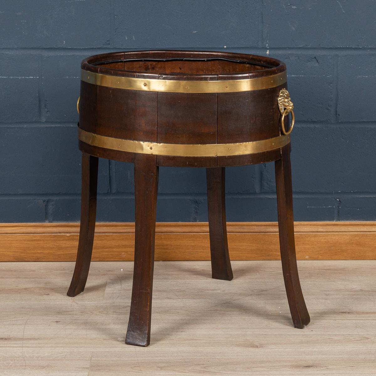 A delightful oak jardiniere or wine cooler made in England around the middle of the 20th century. As is so typical of these items, the jardiniere is constructed with oak slats bound together by a coppered brass band. Slightly splayed legs gives it