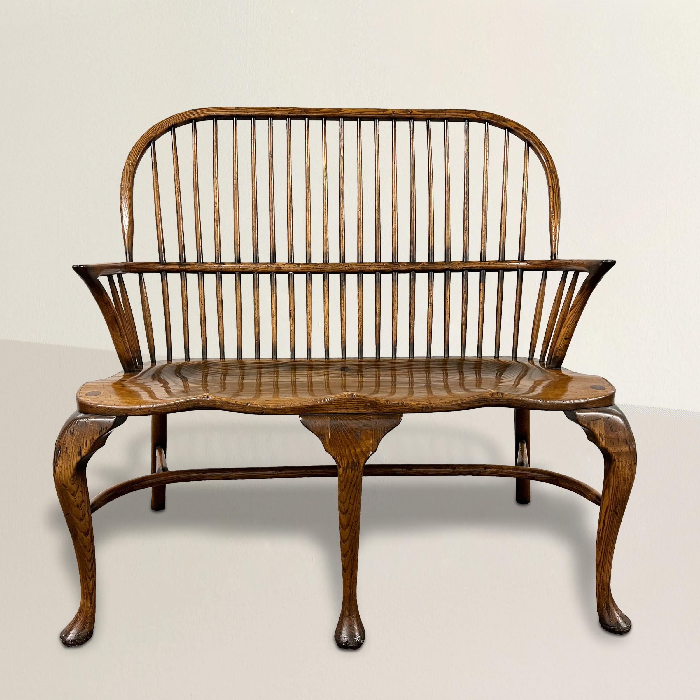 Step into the timeless elegance of this 20th-century English oak Windsor two-seat sack-back bench, a true embodiment of traditional craftsmanship and refined design. Crafted from sturdy oak, this bench showcases the classic Windsor style with its