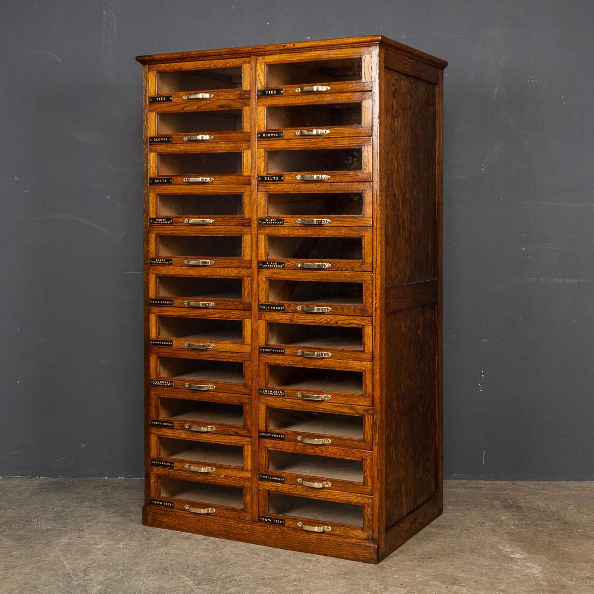 An antique English oak haberdashery with twenty two glass fronted drawers with original brass handles and later painted labels. As functional as it is visually captivating, it not only serves a practical purpose but also stands as a marvellous