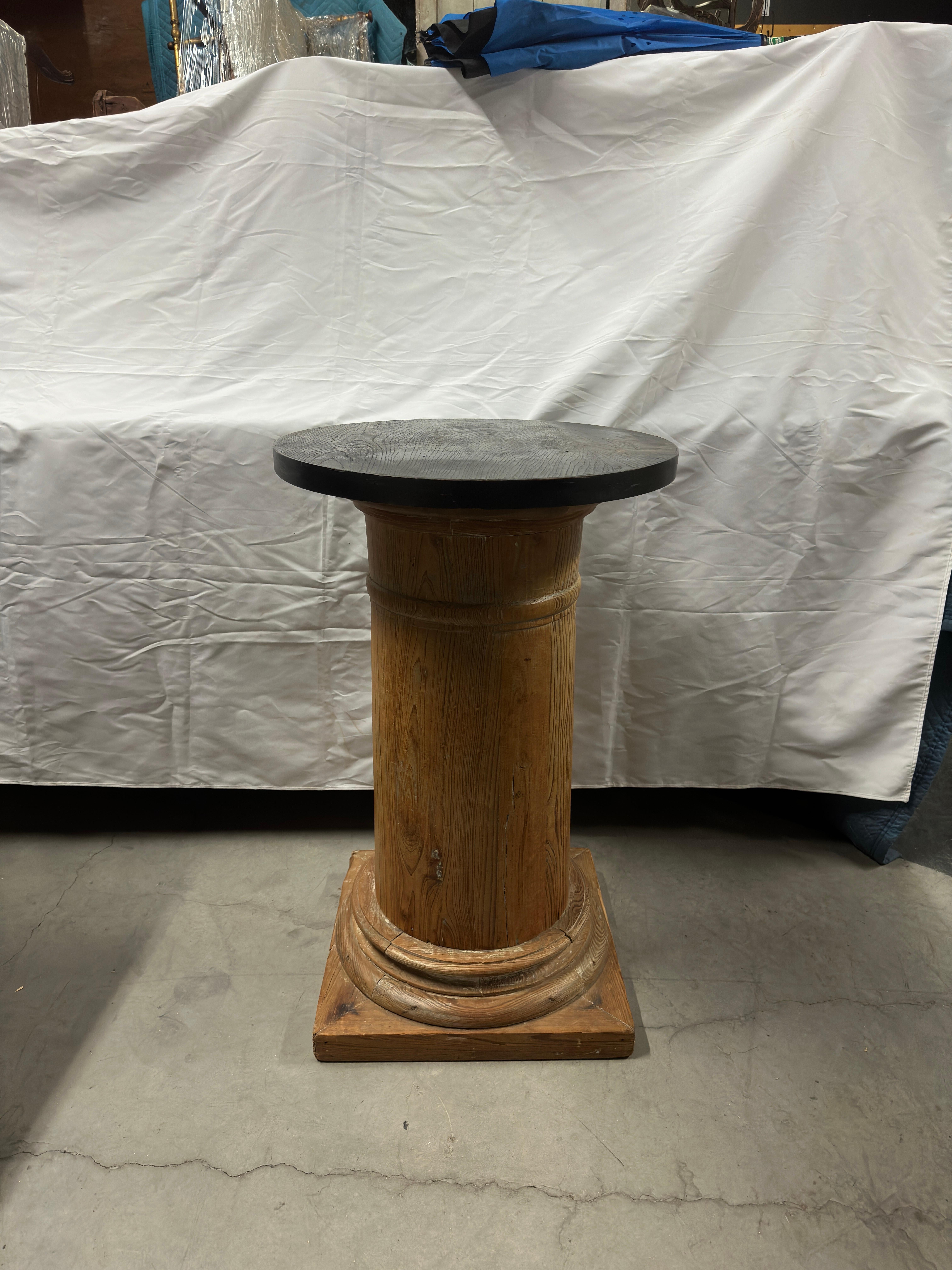 The 20th Century English Pine Column is a unique piece characterized by its distinctive features. It stands tall with a black painted round top, creating a striking contrast against the natural pine wood. The square base provides stability and