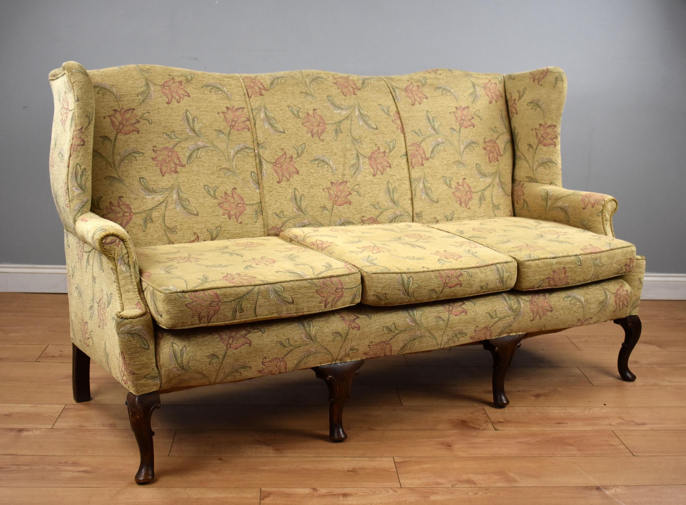 A good quality Queen Anne style wing back sofa, having three seats, above carved and shaped cabriole legs. This piece remains structurally sound and the fabric is in very good condition, showing only light wear to the feet. 

Measures: Width: 72
