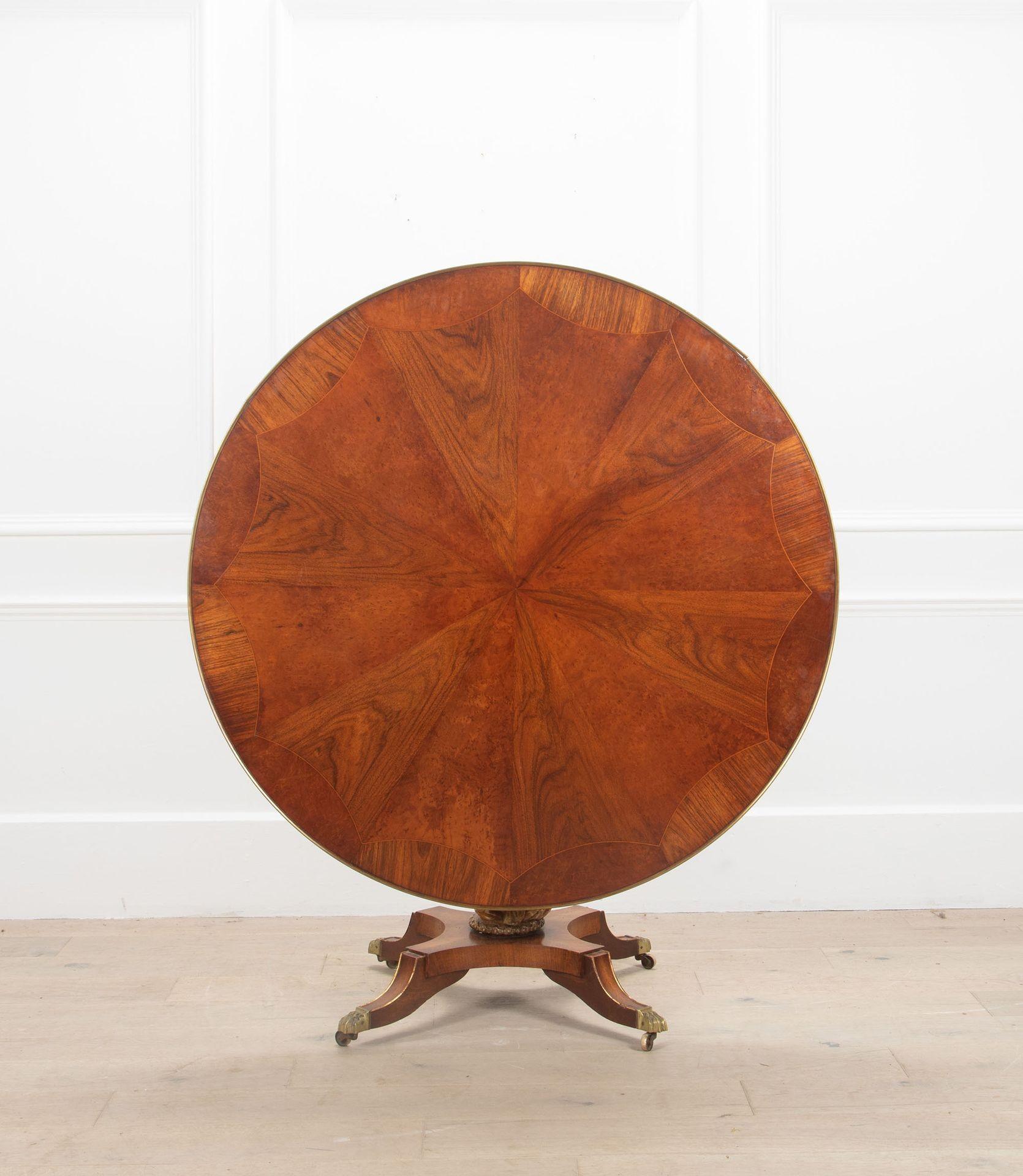 A highly unusual English breakfast or tilt-top table with a radially veneered circular top of exotic timbers bound in brass.

The giltwood column with beautifully carved classical male and female busts sitting on a quatrefoil base raised on sabre