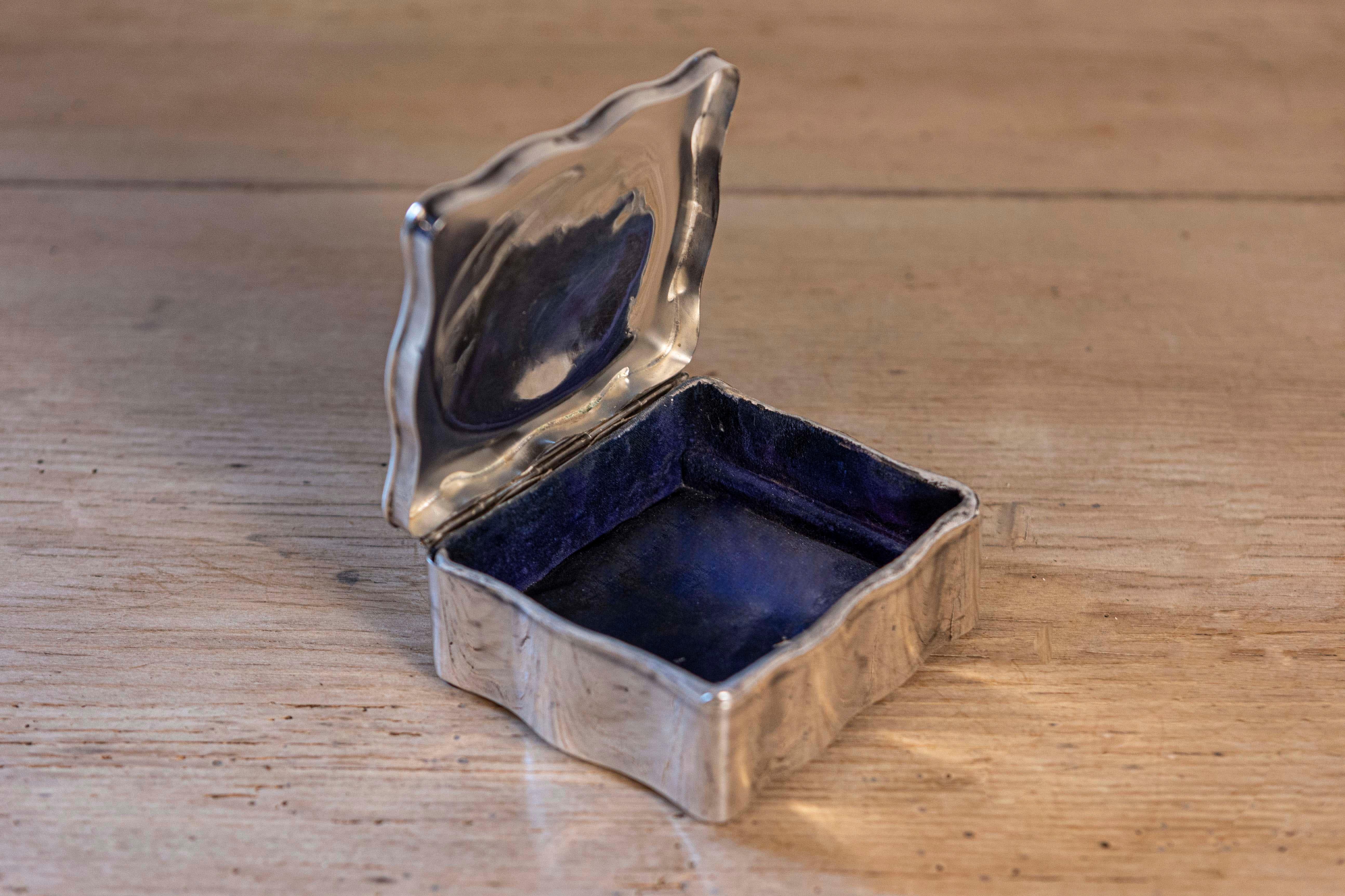 This elegant 20th-century English jewelry box is a fine example of traditional craftsmanship and timeless design. Crafted from sterling silver, the box features a gracefully scalloped edge on the lid, giving it a refined and delicate appearance. The