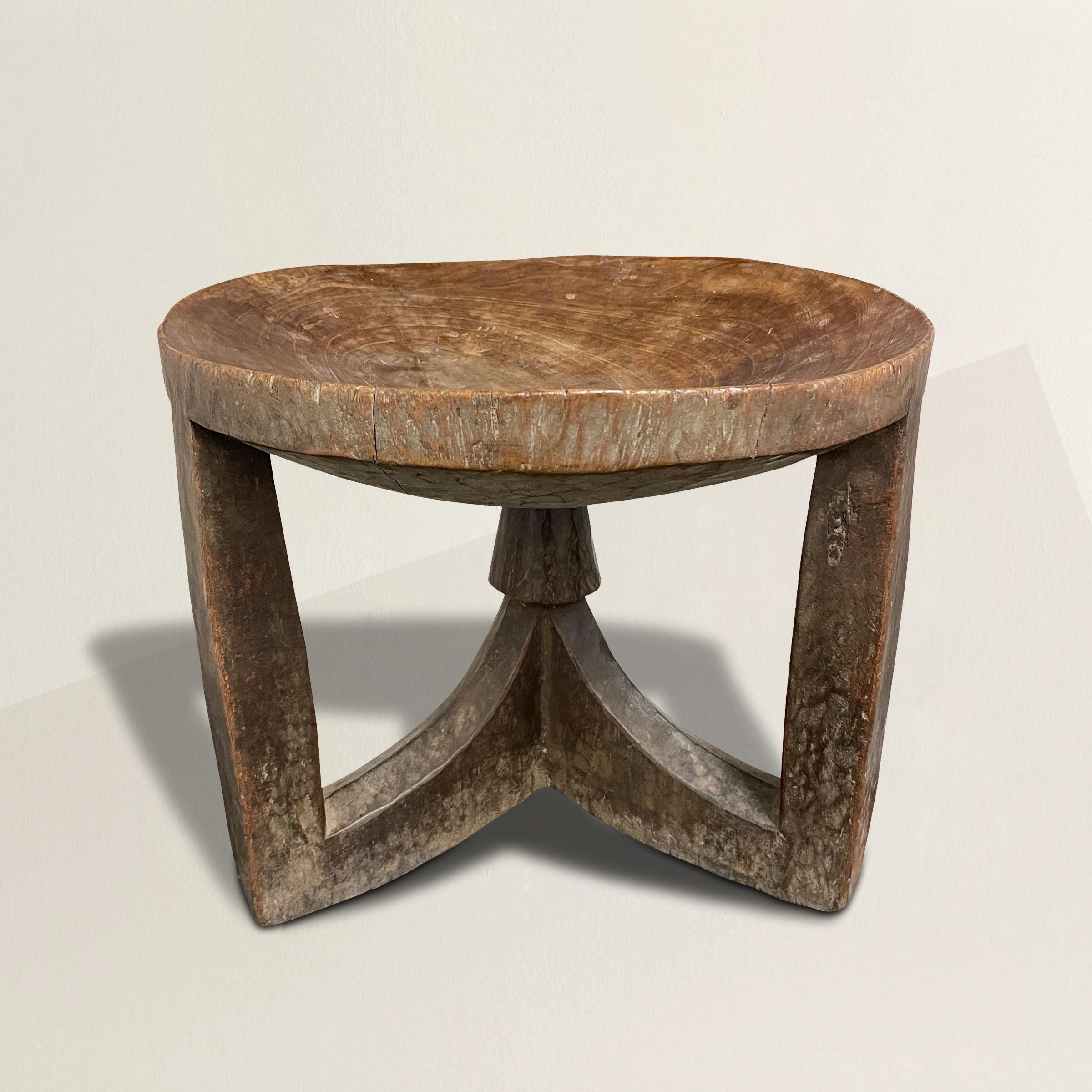 A wonderful 20th century Ethiopian stool carved from one piece of wood, with a concave seat supported by three legs joined in the center. Perfect as a stool, but also doubles as a table next to your favorite armchair.