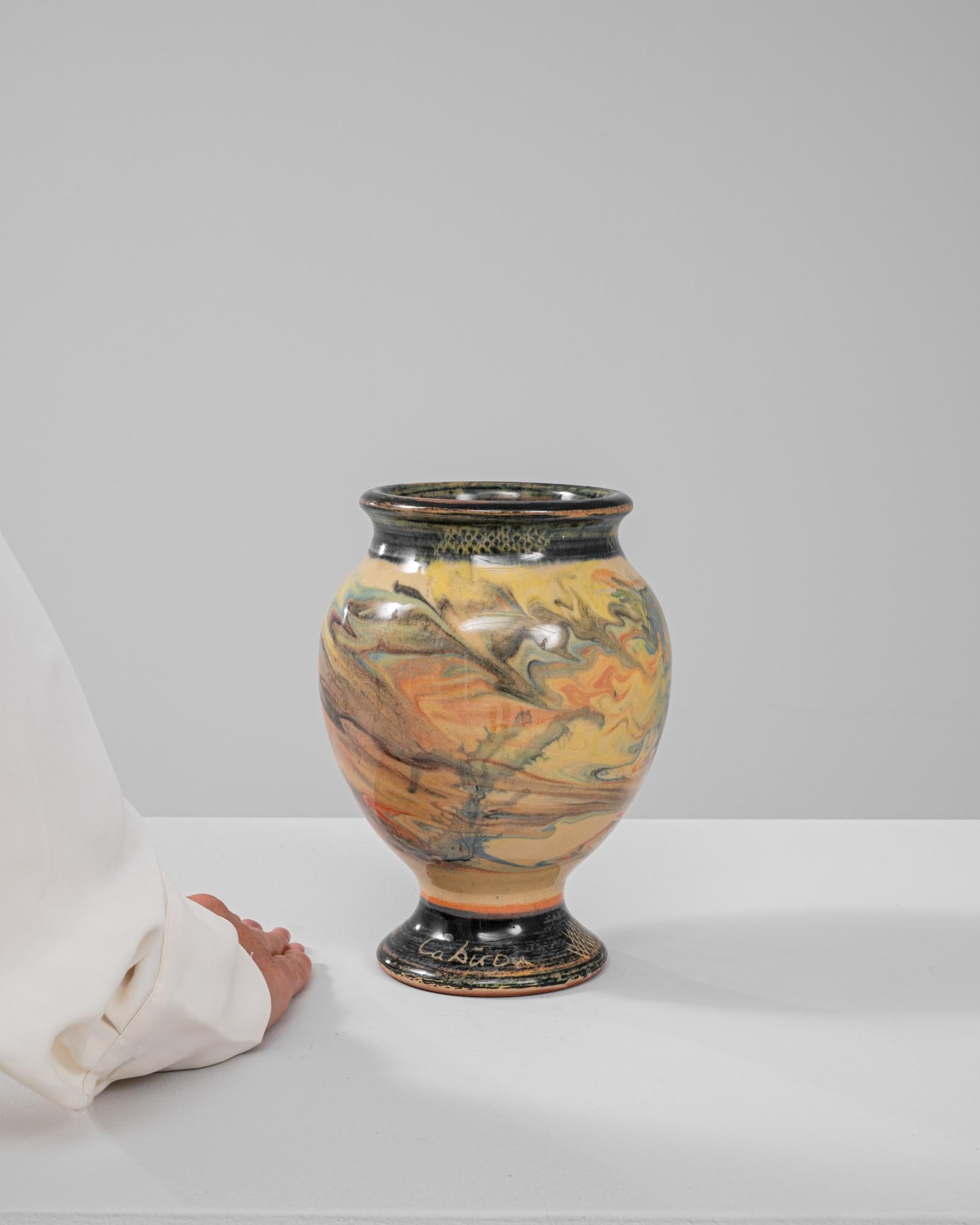 Ce vase exquis en céramique européenne du XXe siècle séduit par son étonnante glaçure marbrée tourbillonnante, mêlant des nuances de jaune, d'orange, de vert et de brun terreux en un motif hypnotique et unique en son genre. Le vase présente un corps