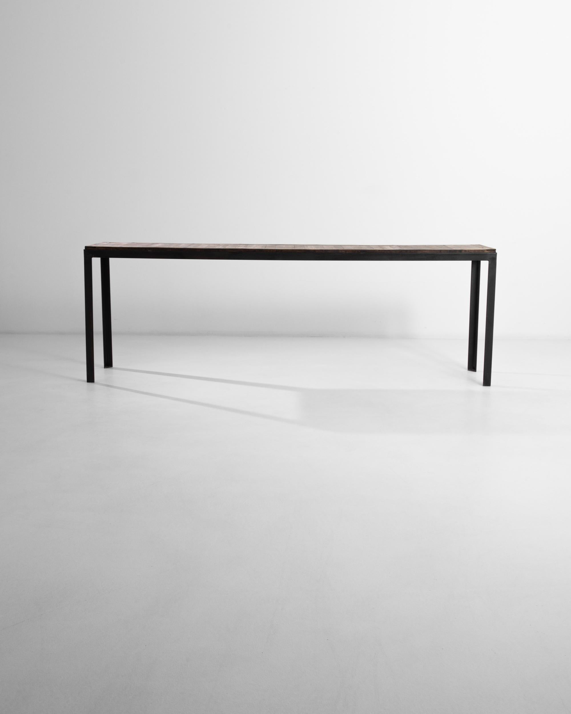 Composed with 20th century architectural salvage from France, this table boasts an industrial steel frame that elevates a wooden table top. The texture of the raw wood enhances the crude minimalist aesthetic of the black-patinated metal base. High