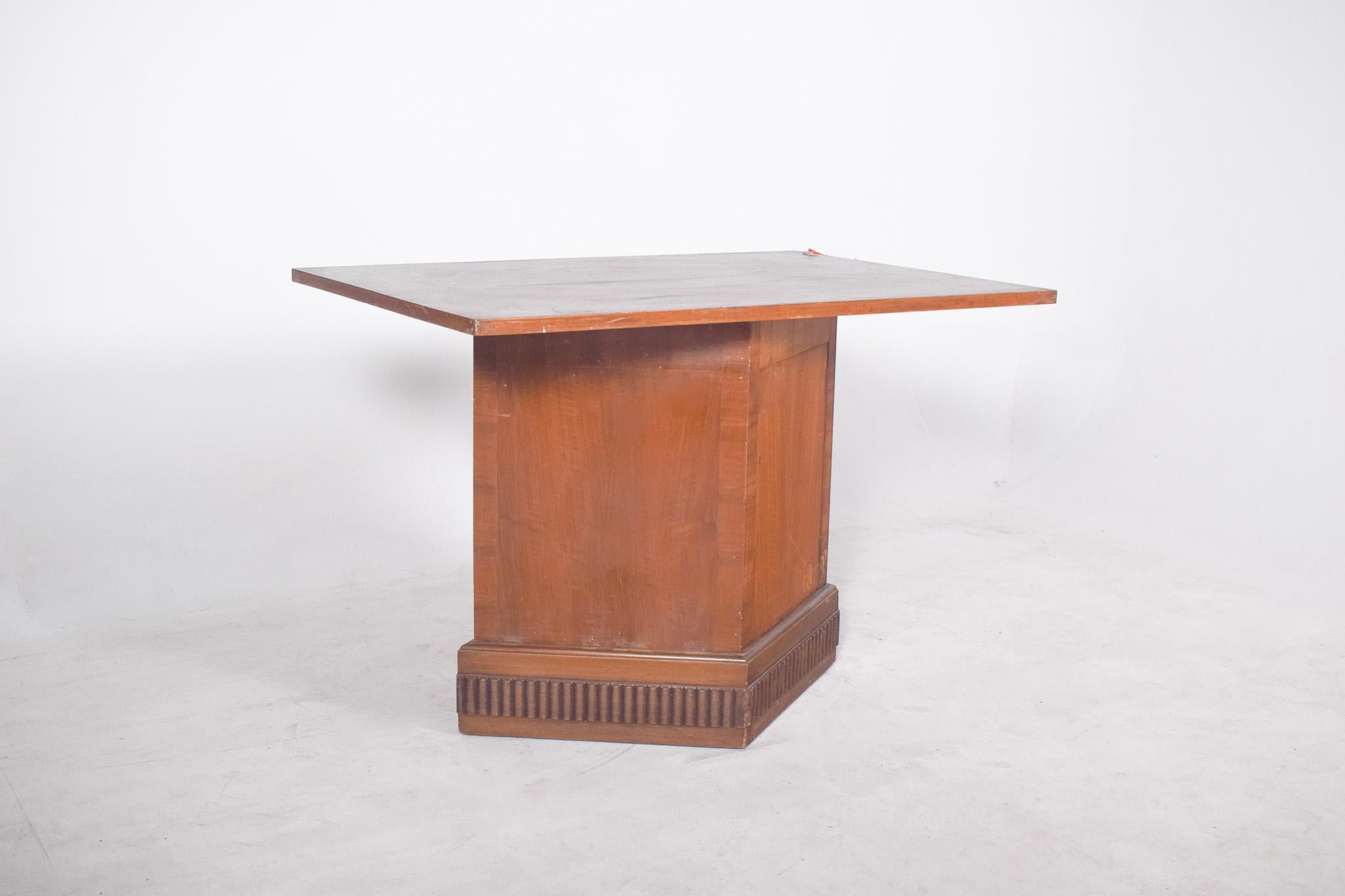 Table with base unit and door. With a unique design, the central base is robust and trapezoidal in shape, giving the furniture stability and grandeur. The structure is made entirely of wood, finished in a medium tone with visible veins, which