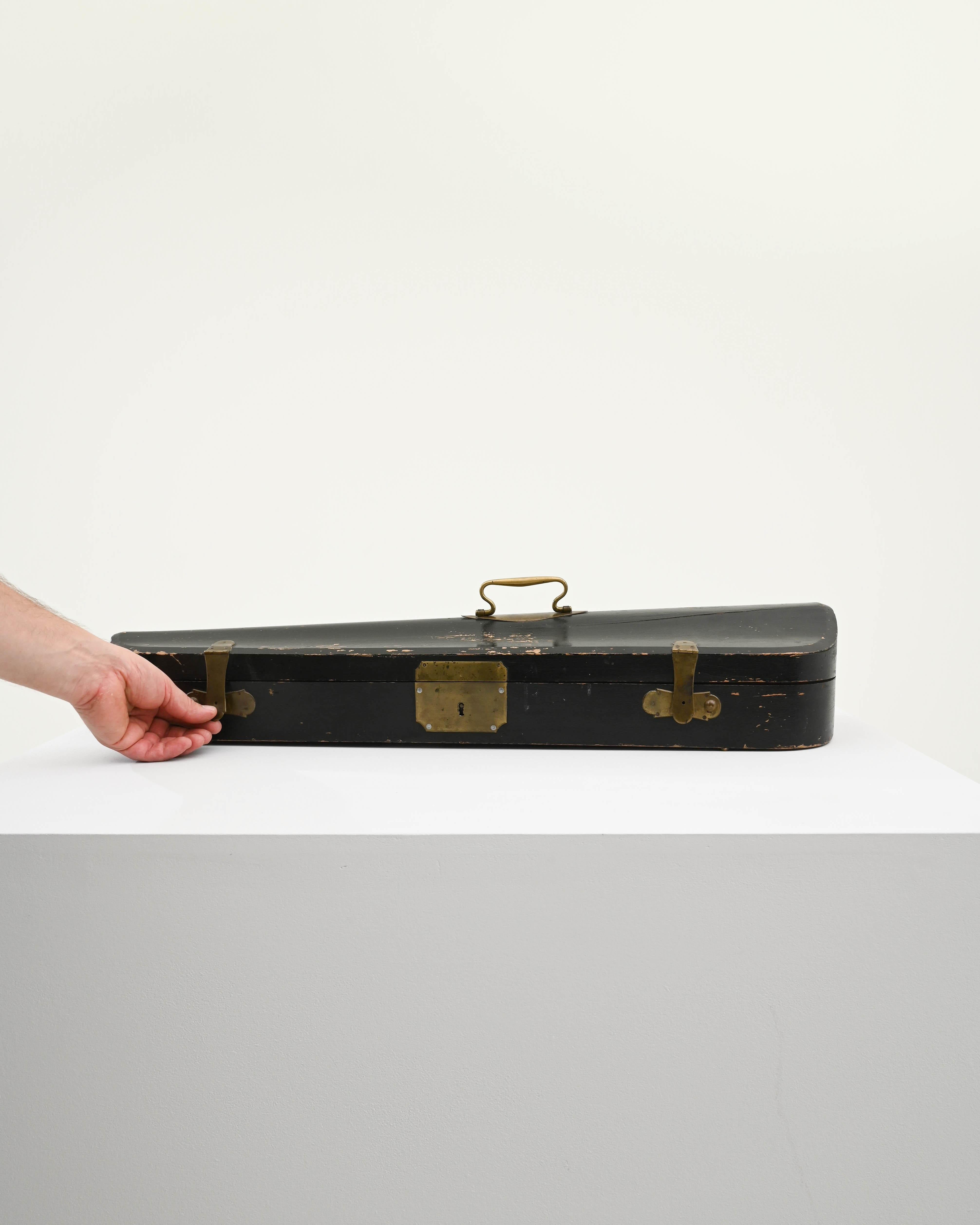 Made in Europe in the 20th Century, this vintage wooden case would have originally been used to hold a musical instrument—the distinctive shape suggests a violin. The wood has been painted in a sober black hue; elegant brass clasps and a gracefully