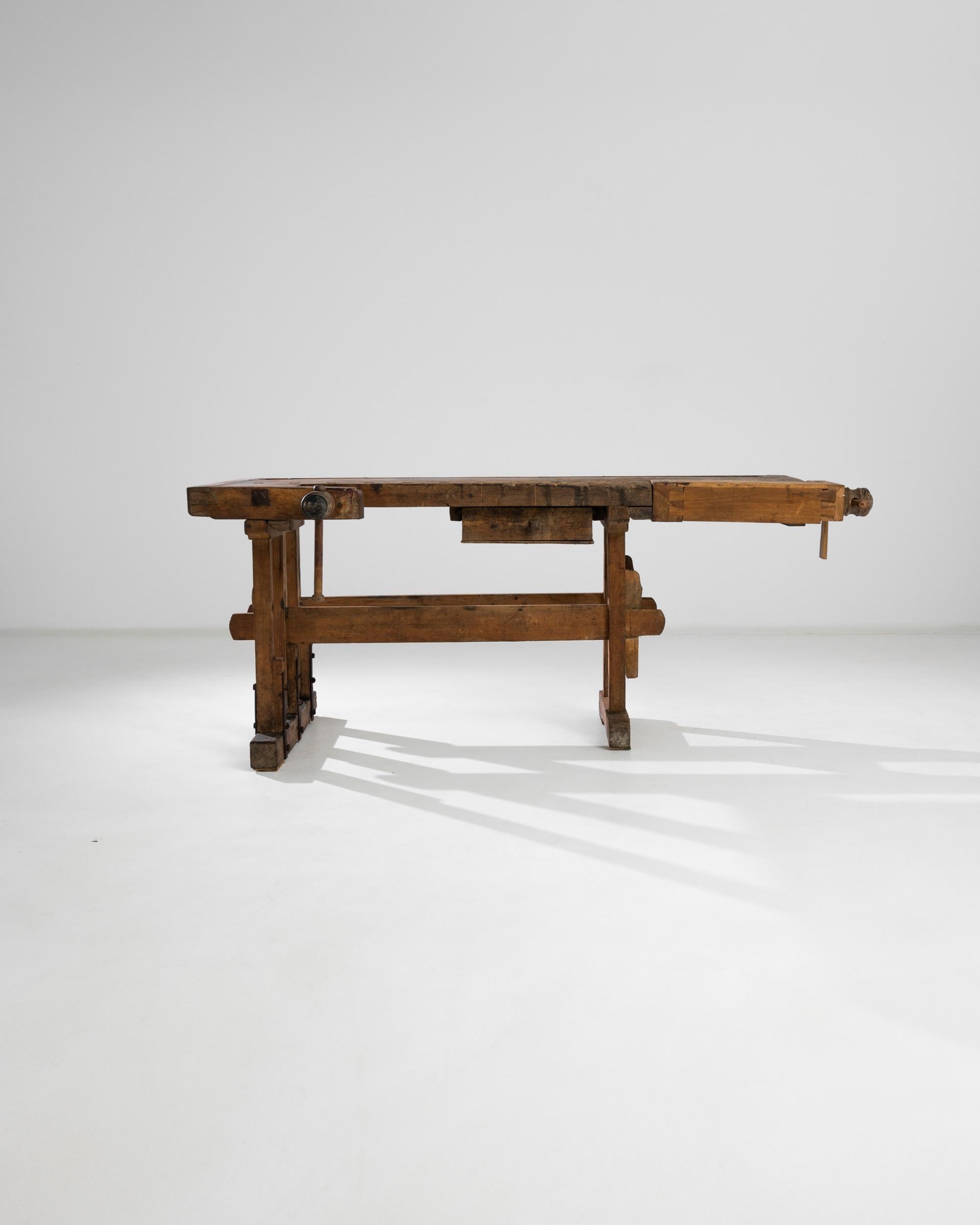 A 20th century woodworking workbench from Central Europe, this mechanical jewel bears the marks of skilled craftsmanship. This antique wooden carpenter’s workbench displays English dovetail hewn joints, two wooden working screw vices, a deep tray