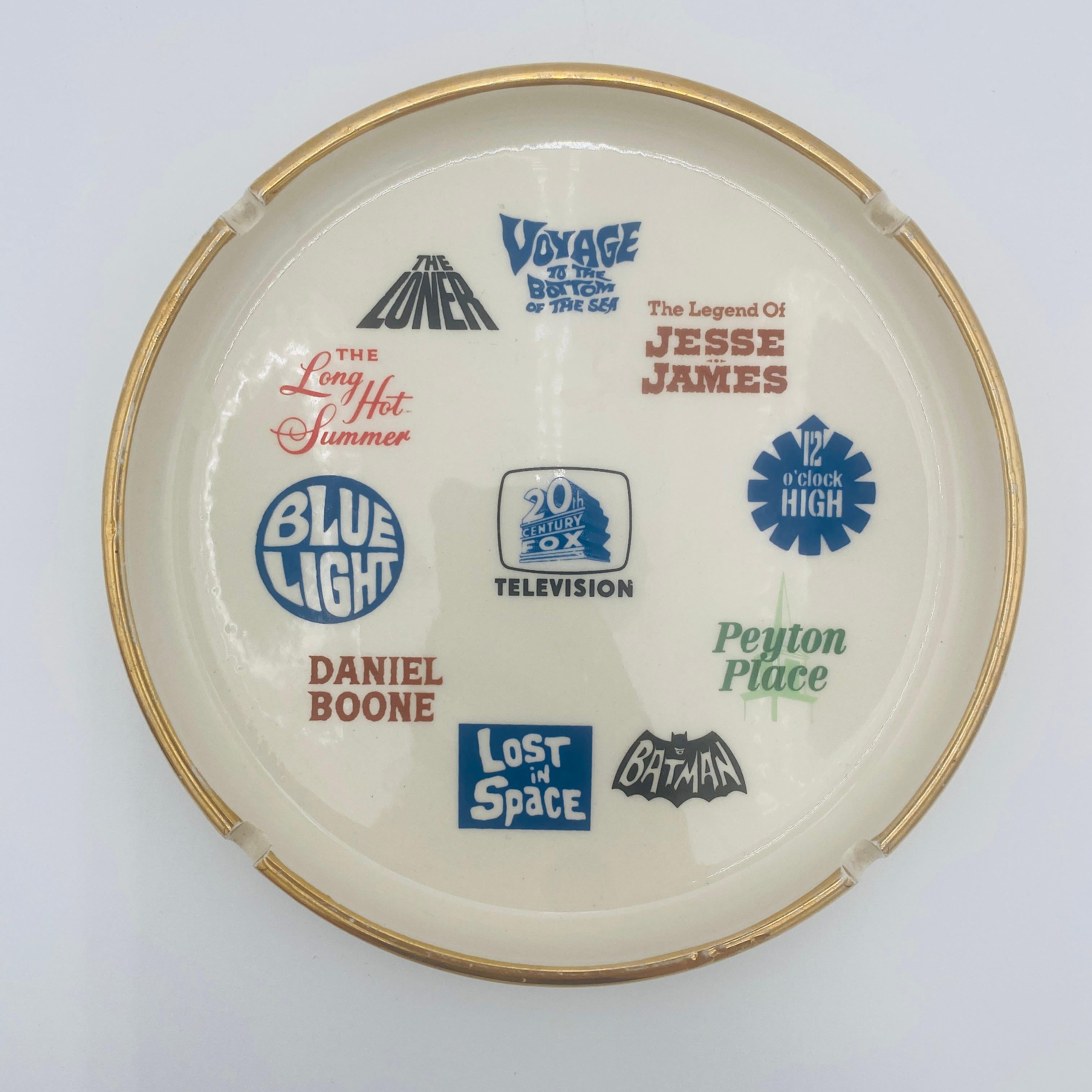 Questo posacenere in ceramica smaltata con bordo dorato presenta il logo 