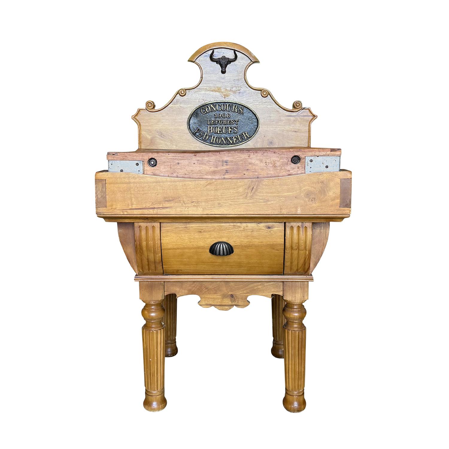 An early 20th Century, antique French butcher block table in solid Beechwood, featuring a richly aged cutting surface and turned, fluted legs, in good condition. The piece is crowned with an ornate backplate, prominently displaying a cast metal