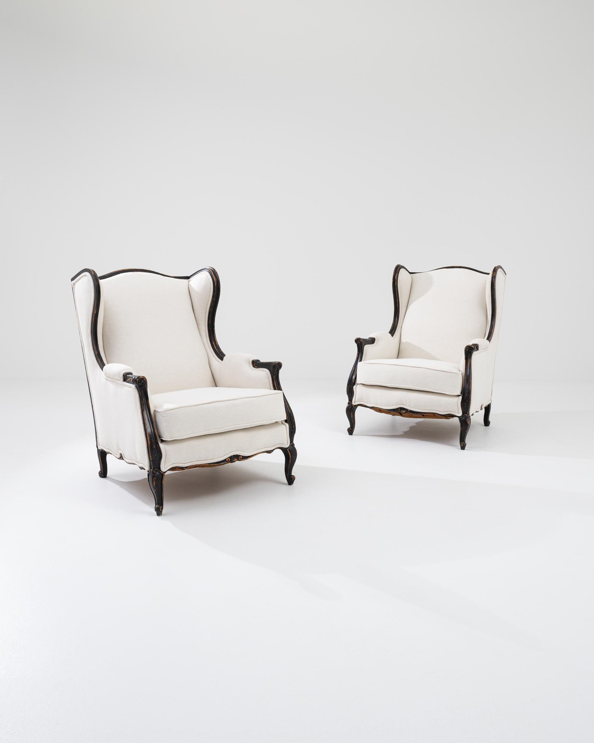 This grand pair of winged armchairs offer an irresistibly comfortable seat. Made in 20th century France, the shape takes inspiration from the traditional wingback chairs of centuries past, originally designed to create a cocoon of warmth from the