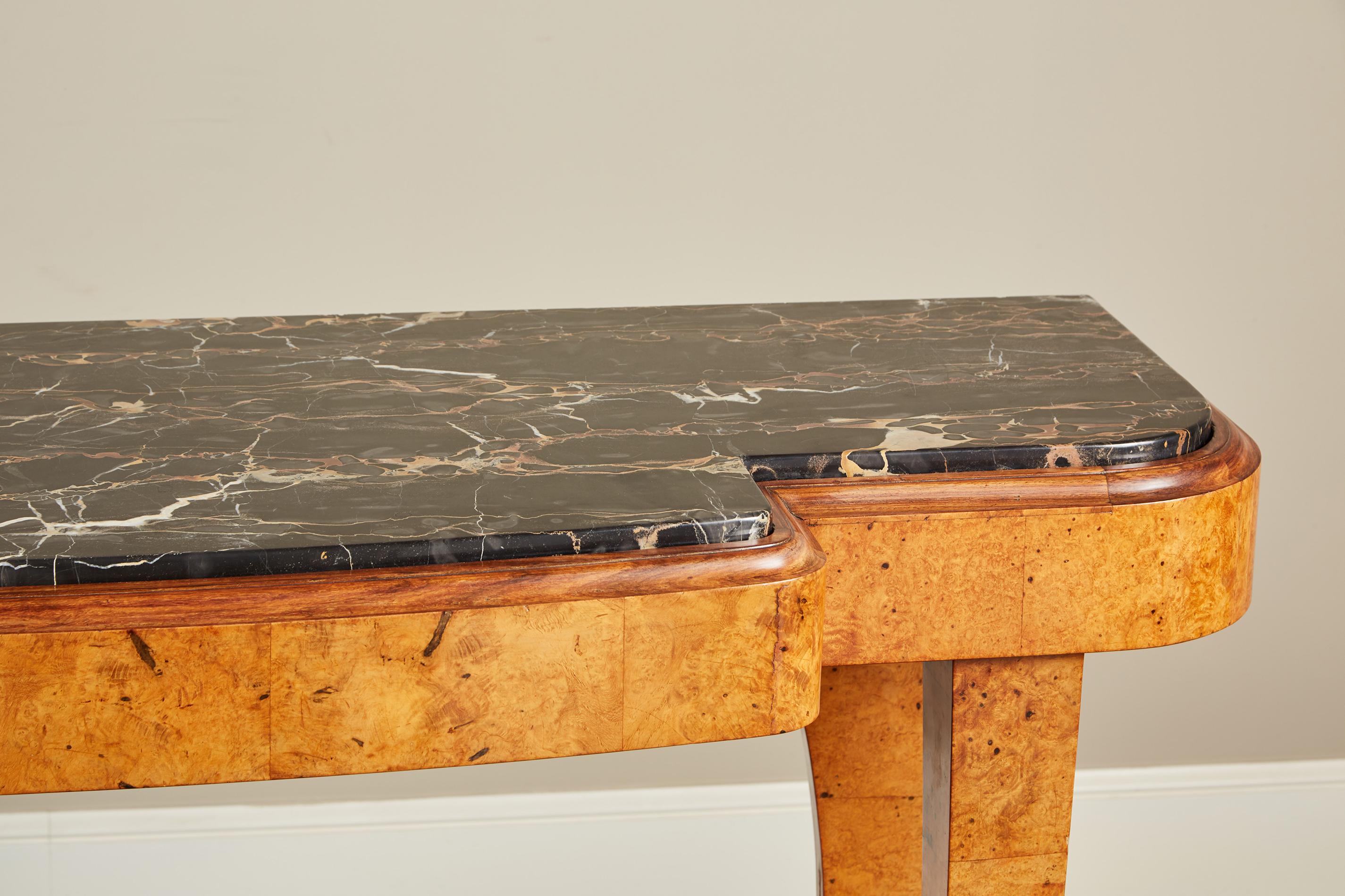 A remarkable French Art Deco console table. The break-fronted top with curved corners, made of white and pink-veined black marble, rests on an apron and legs of burl wood. The rectangular-section front legs curve inwards before flaring at the base,