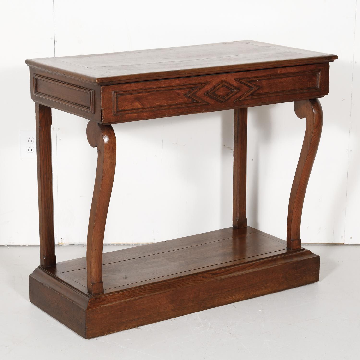 French Art Deco period console handcrafted in solid oak, having a rectangular top sitting above a single carved drawer flanked by scrolling columnar supports terminating in small hoof feet, all raised on a conforming plinth. The graceful curves and