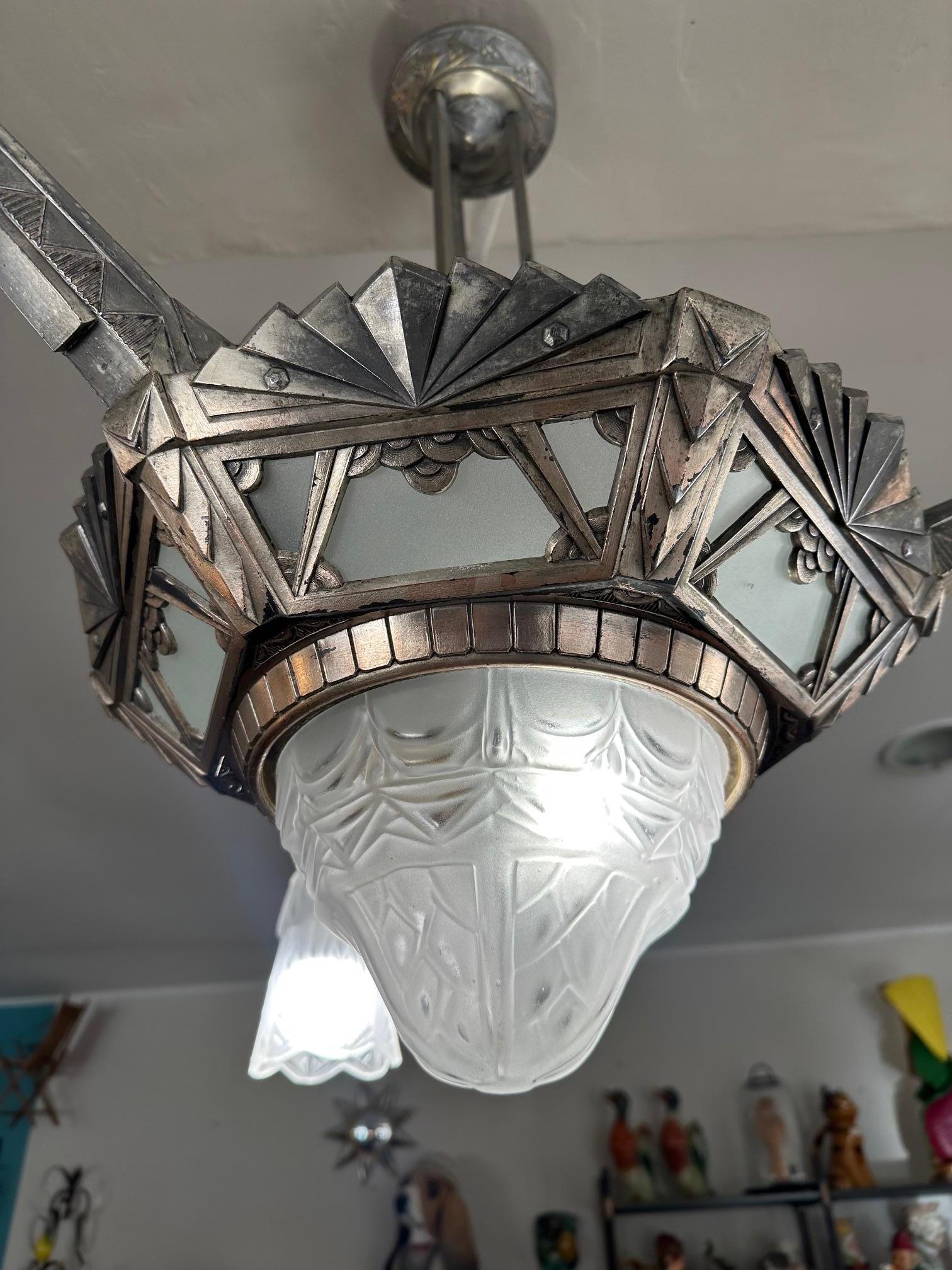 Magnifique lustre en bronze argenté datant de la célèbre période Art Déco (1930) en très bon état.
Il présente des formes géométriques typiques de cette époque.
Ce lustre est composé de trois abat-jour en forme de tulipe et d'un globe central