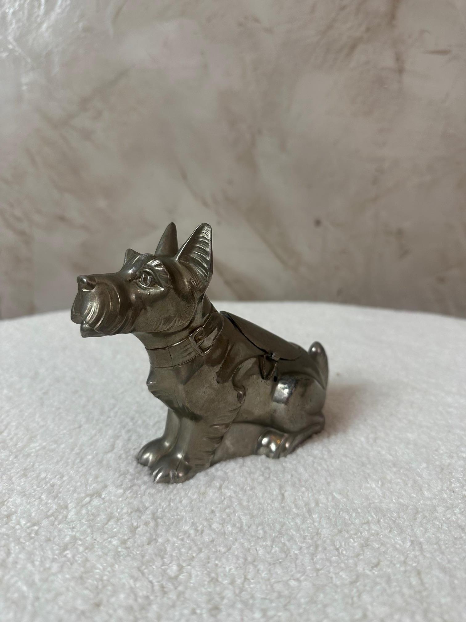 Preciosa hucha vintage con forma de perro sentado, fabricada en metal plateado en la década de 1930.
Su diseño Art Déco y su carácter expresivo lo convierten tanto en un objeto decorativo como en una pieza de colección.

El perro está finamente