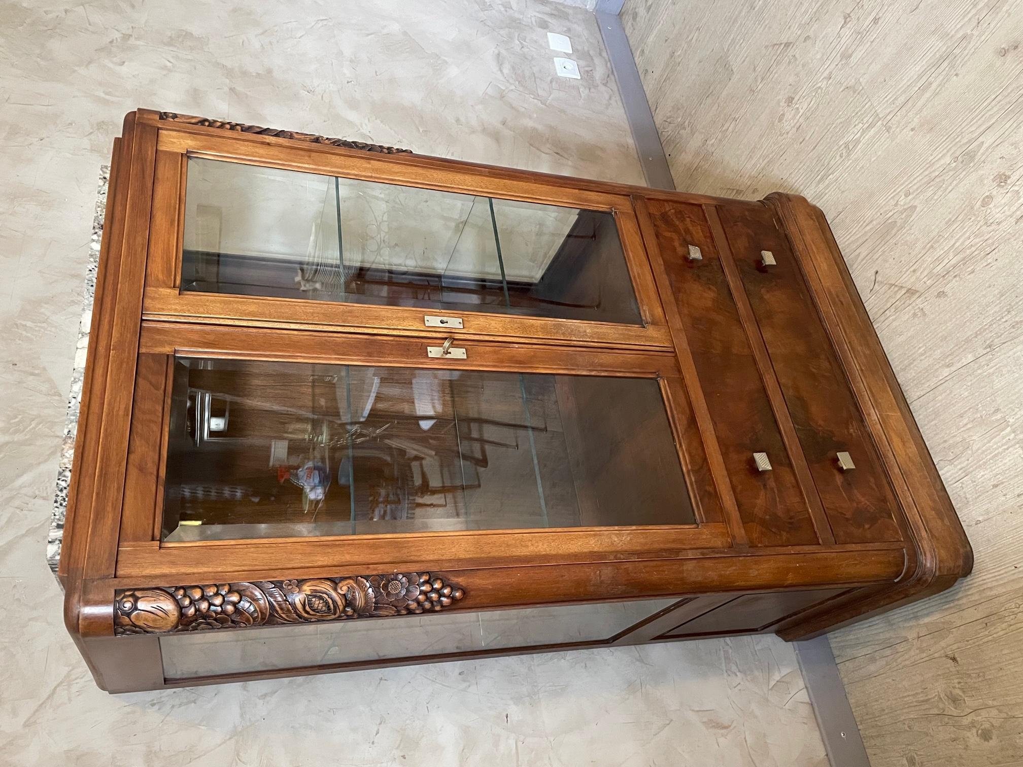 Very beautiful and rare small Art Deco vitrine in walnut.
Flowers engraved in the wood which represents the 1930s period. 
Bevelled glass doors and sides. Two glass shelves.
Two large drawers on the bottom with brass handles.
Marble top on top.