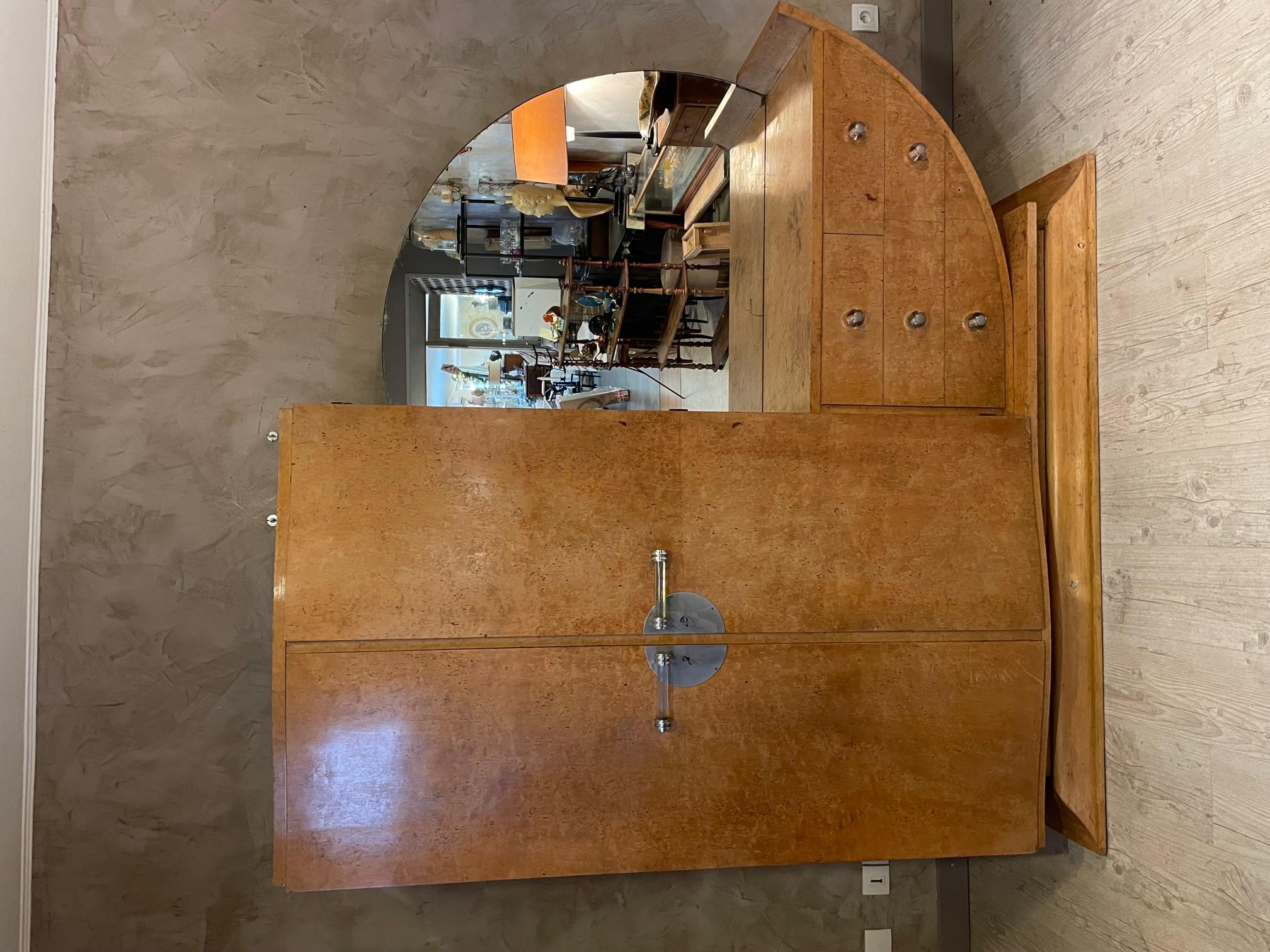 Very nice Art deco Birdseye maple wardrobe from the 1930s. 
On the left side, there are two doors with beautiful glass and chromed metal handles opening on a wardrobe and many shelves. 
On the right side, we can see a large rounded mirror and three