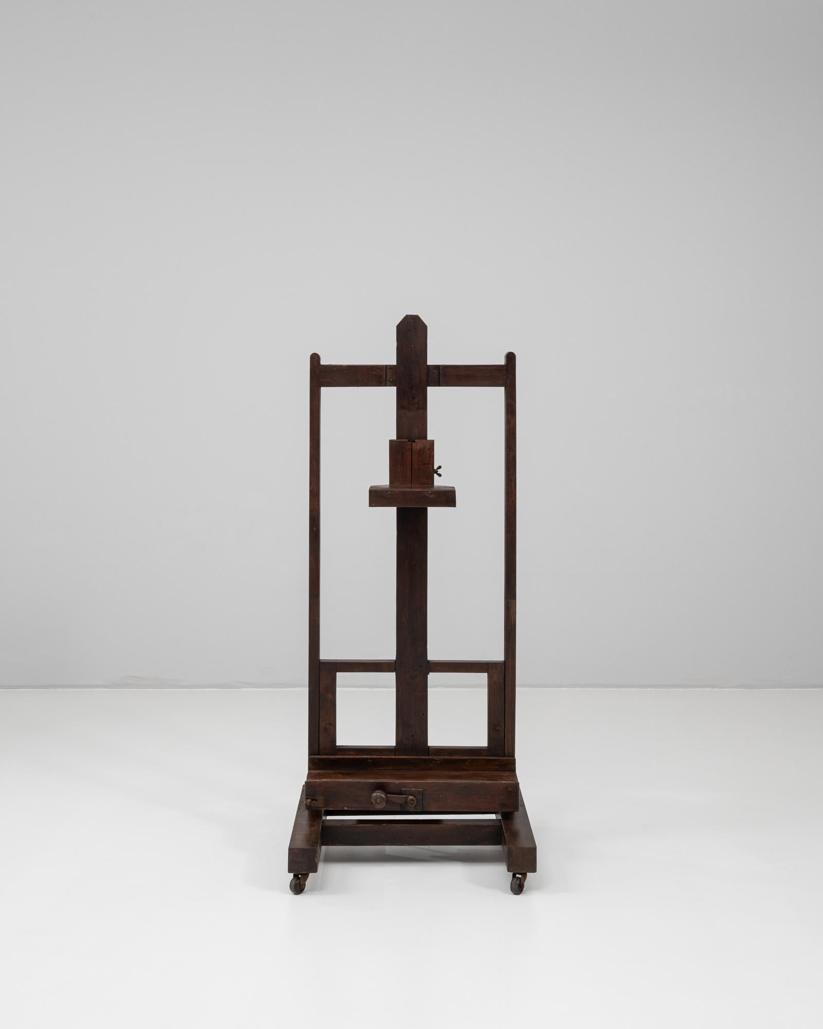 Ce chevalet d'artiste français du XXe siècle incarne le savoir-faire et l'aspect pratique des meubles d'atelier traditionnels. Construit en bois massif à la patine riche et foncée, il est doté d'un mécanisme de hauteur réglable et d'une base à