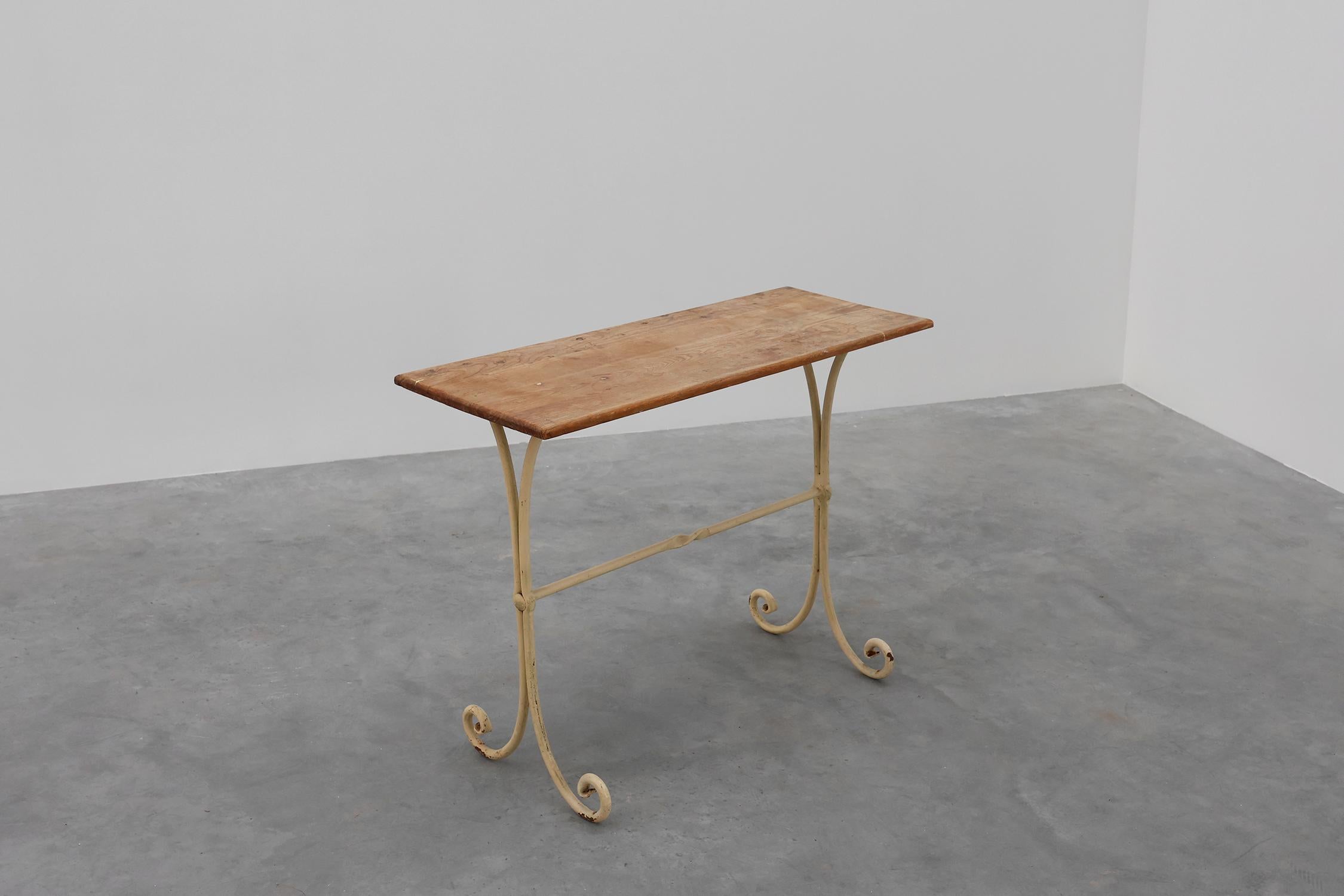 Belle table de bistrot française du début du 20e siècle. Cette table a un plateau rectangulaire en bois de chêne massif et une base en fonte avec de vieilles couches décoratives de peinture couleur crème et altérée par les intempéries. Cette table