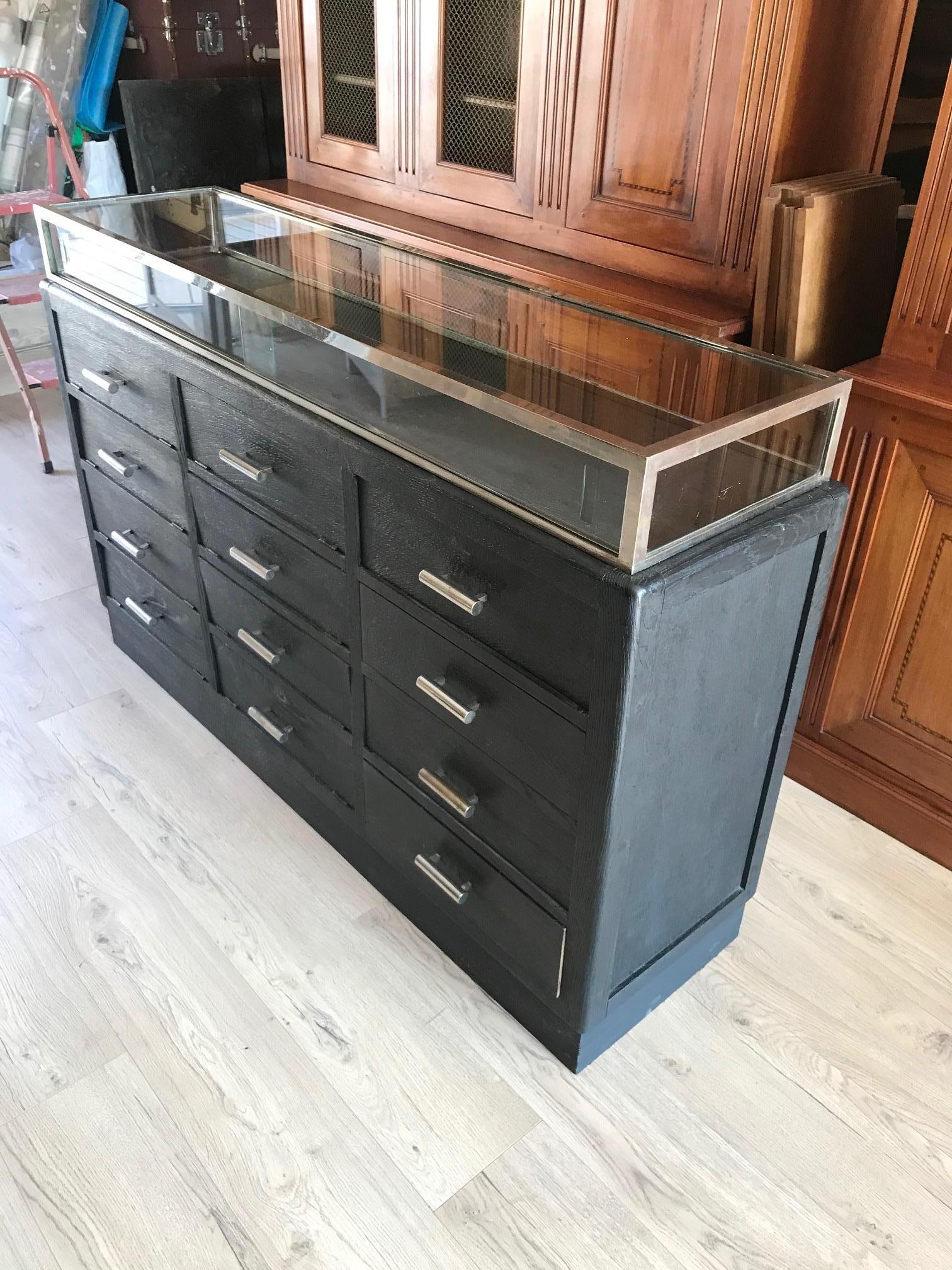 Beautiful and rare 20th century French black painted chest of drawer apothecary cabinet from the 1900s. 
Glass vitrine on the top with two sliding doors. 
Multiple drawers with three racks, maybe used to present gloves or shirts and there is