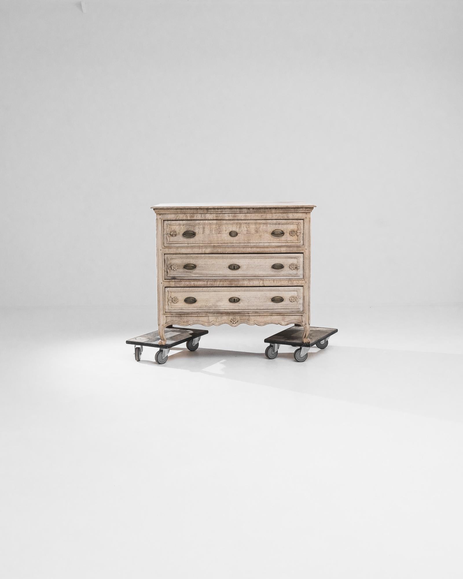 This elegant three-drawer chest features graceful cabriole legs adorned with meticulously carved accents that continue onto the scalloped apron. Created in France during the 20th century, this dresser was handcrafted from oak that has been