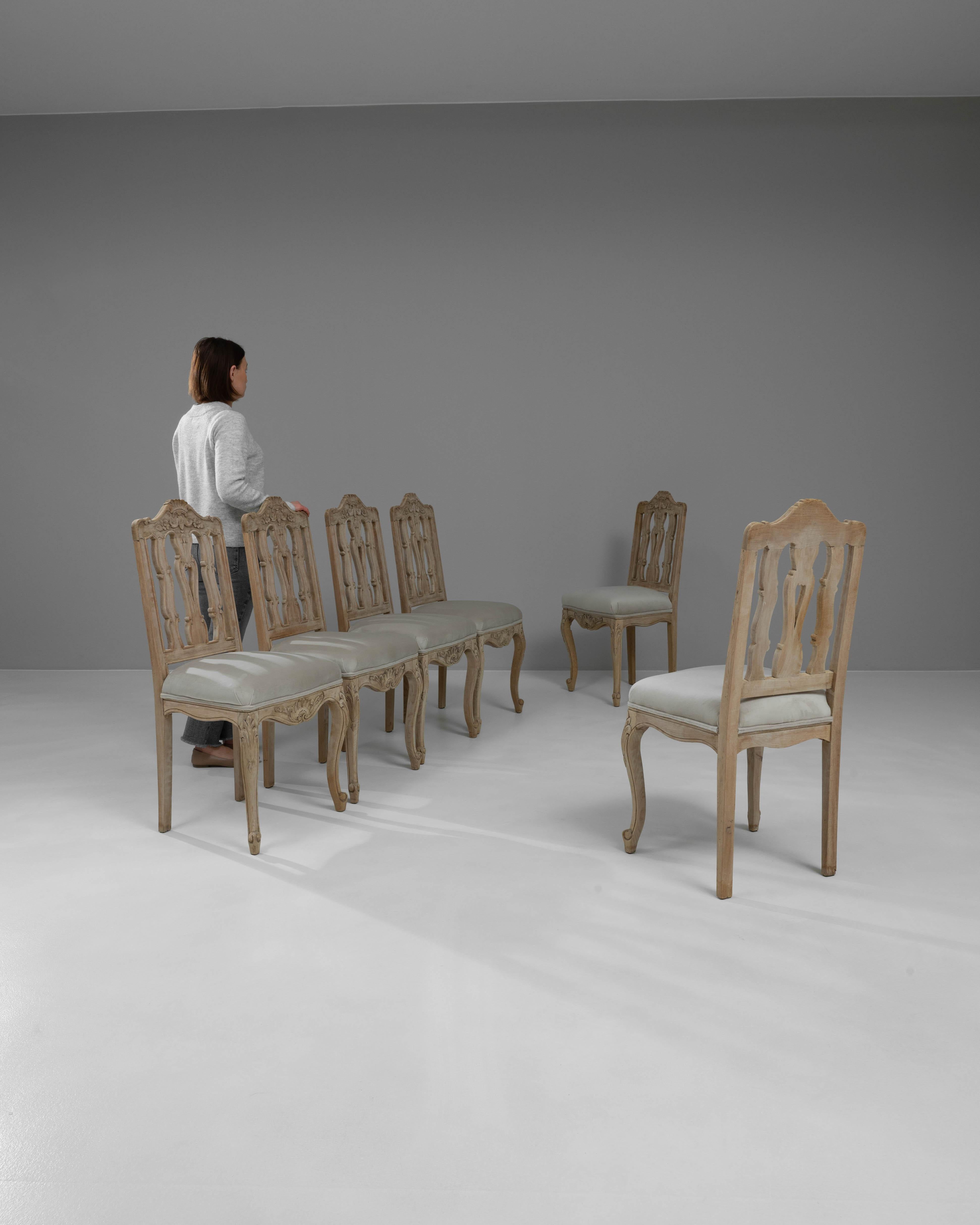 Elevate your dining experience with this exquisite set of six 20th Century French Bleached Oak Dining Chairs, each piece a testament to classic design and refined craftsmanship. These chairs feature intricately carved backs that showcase floral
