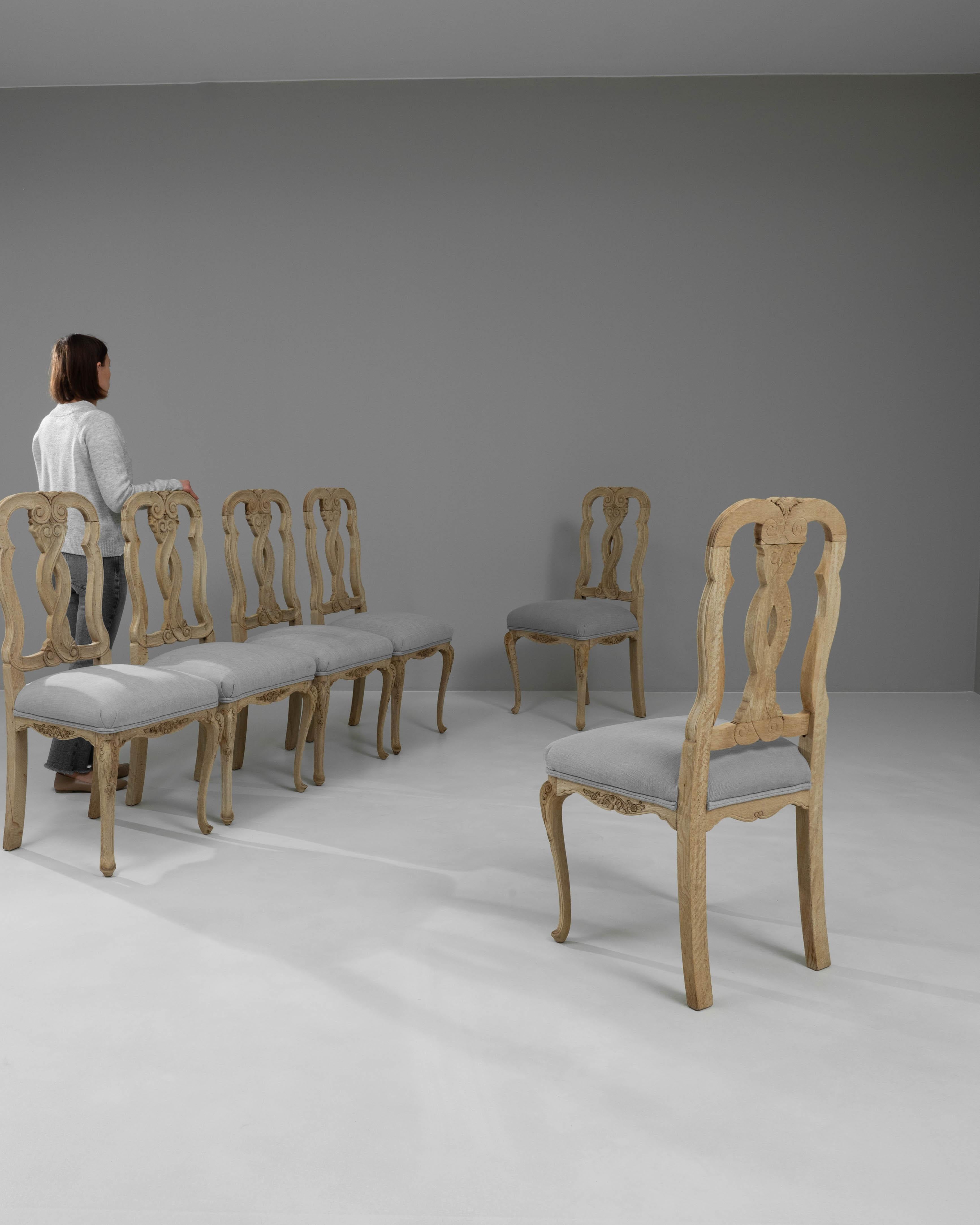 Introducing a magnificent set of six 20th Century French Bleached Oak Dining Chairs, each piece artfully crafted to bring timeless elegance into your home. With their graceful silhouettes and expertly carved sinuous details, these chairs capture the