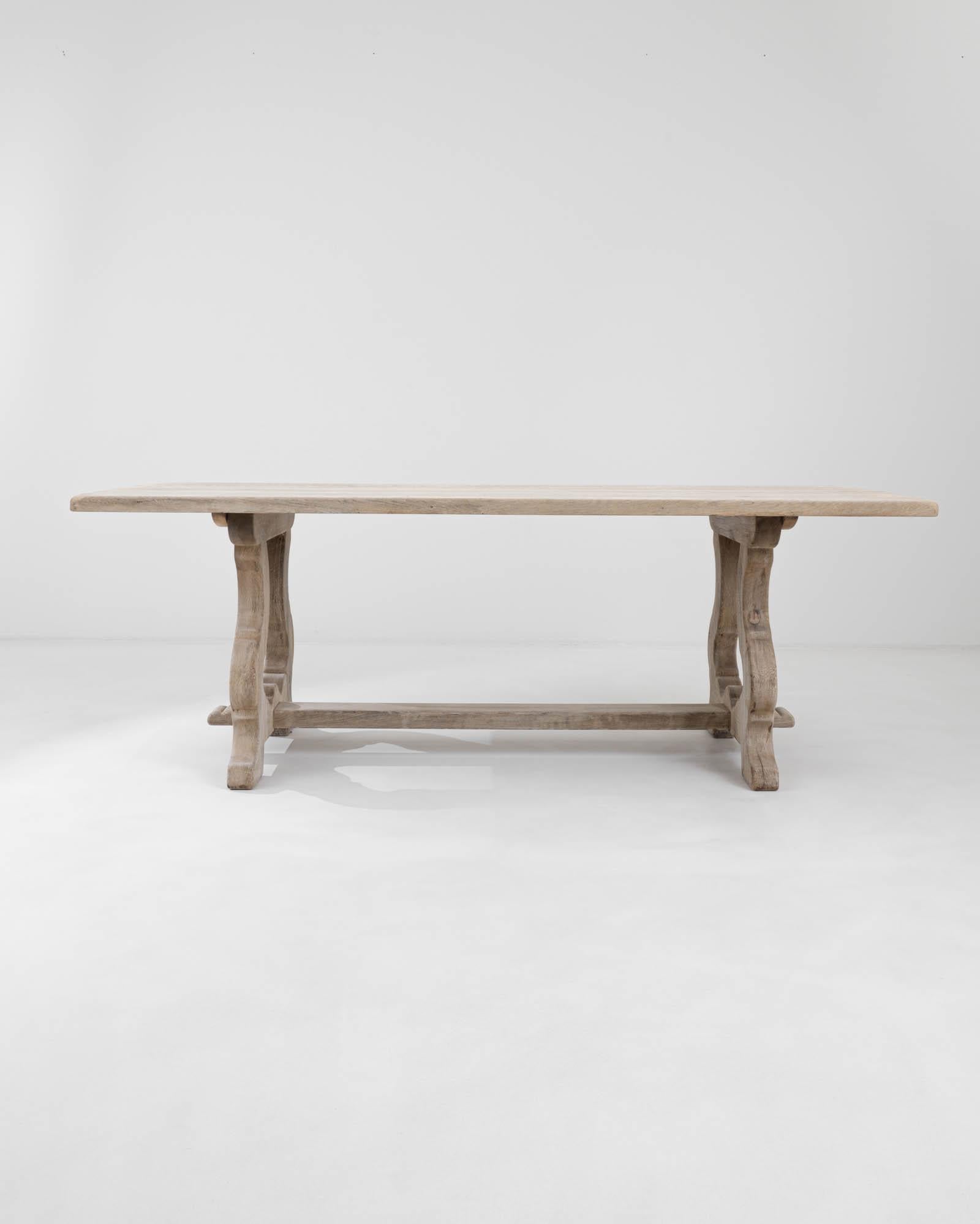 The gracefully flowing outlines of the carved trestle legs define the captivating silhouette of this oak dining table, while offering robust support. Handcrafted from solid European oak in 20th-century France, this table showcases a lengthy, smooth