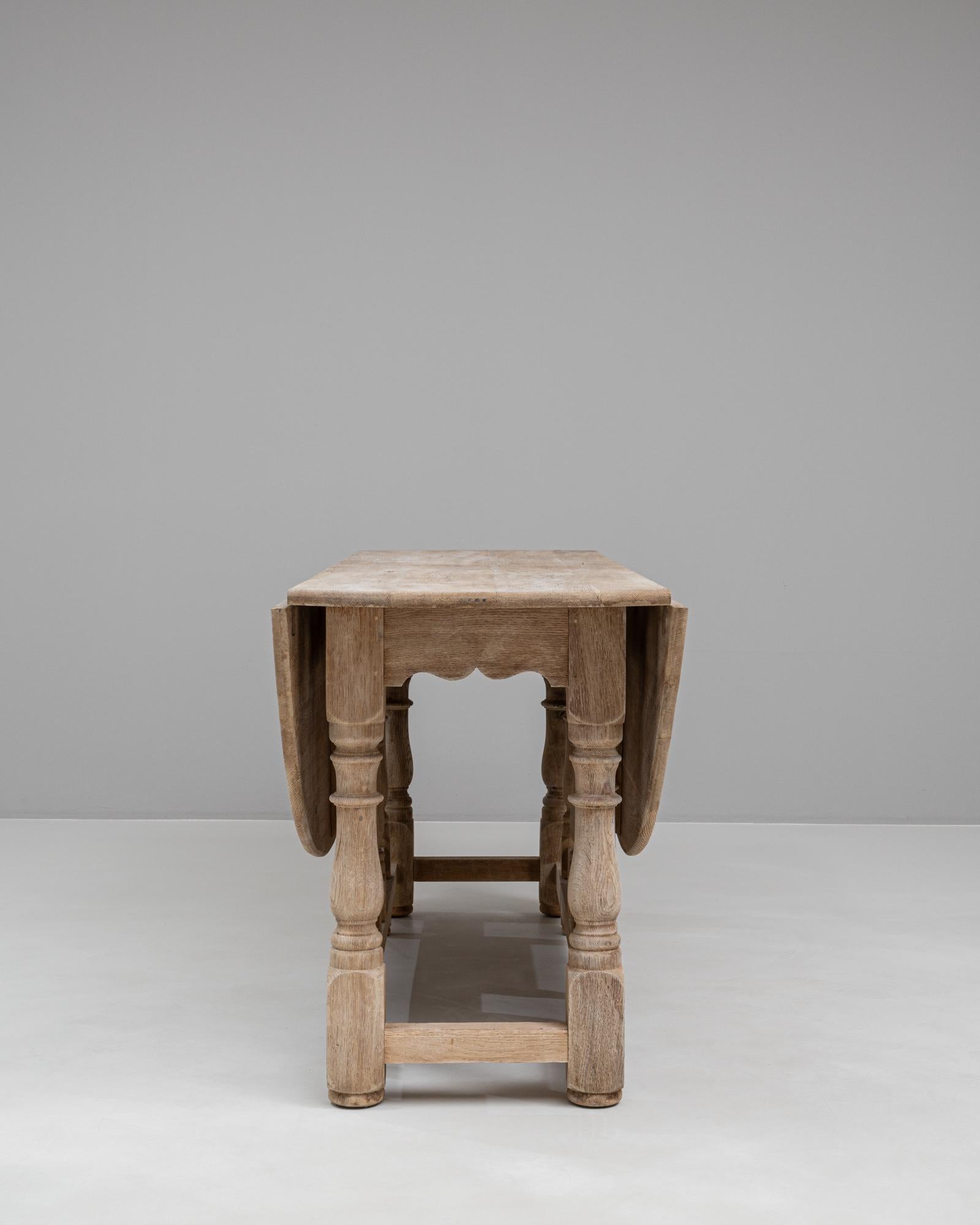 Enhance your home with the elegance and versatility of this 20th Century French Bleached Oak Drop Leaf Table. Expertly crafted from solid oak, this table features a beautiful bleached finish that highlights the natural grain and texture of the wood.