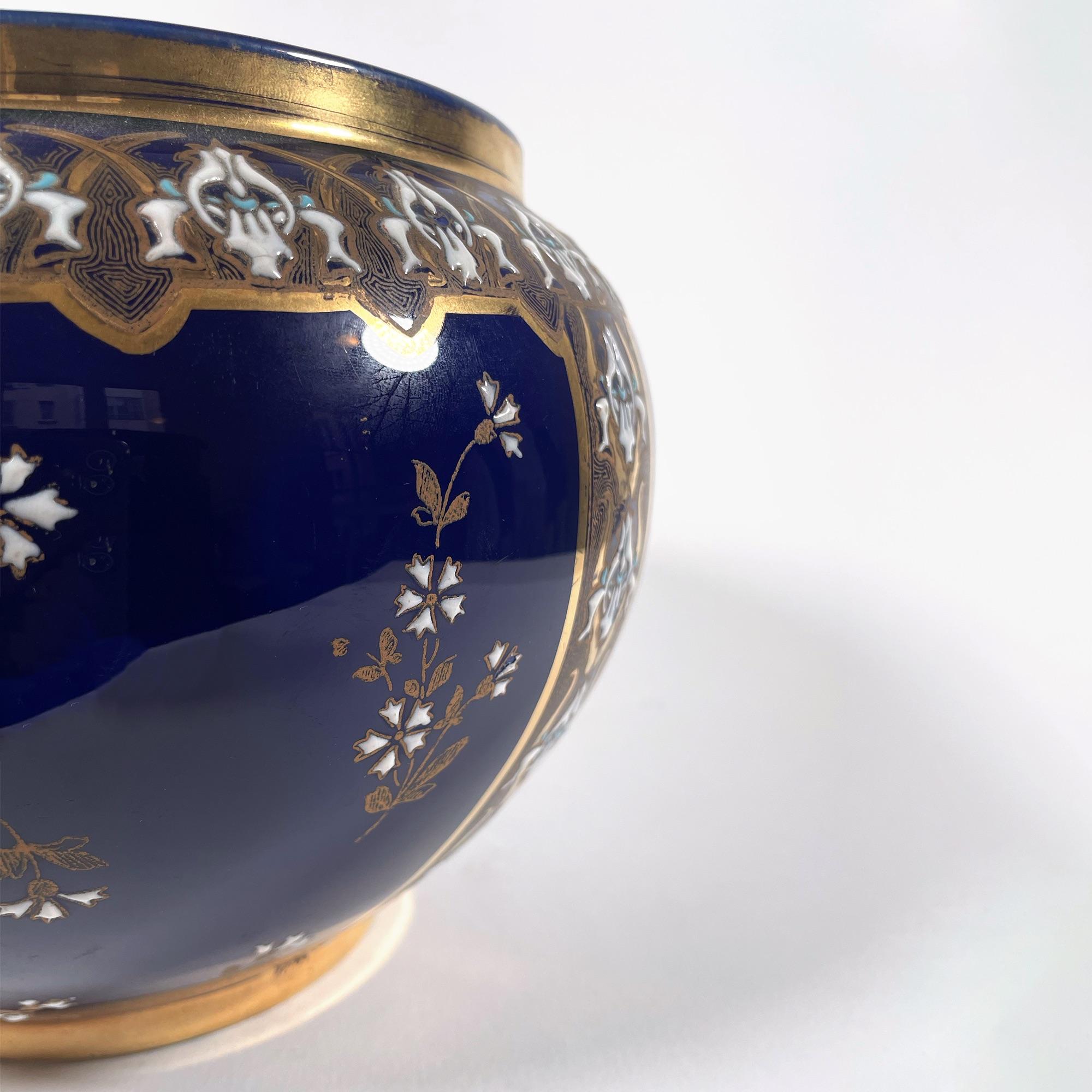 This exquisite French faience cachepot from the renowned R&G Lunéville workshop is a timeless decorative piece. Crafted in the 20th century, it features a deep blue glaze accented by a delicate white and gold frieze, adorned with elegant cornflower