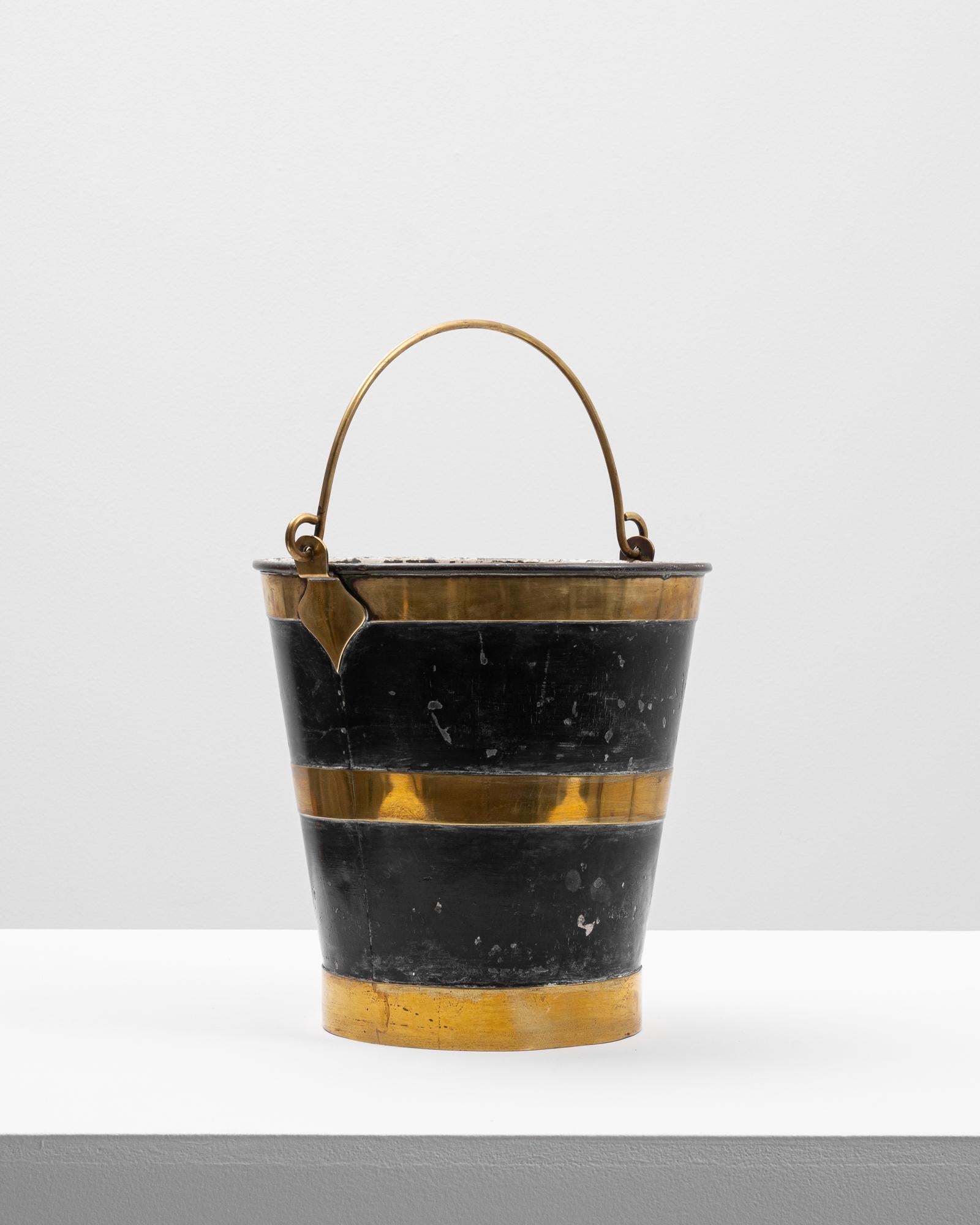 This 20th Century French brass bucket offers a handsome blend of utility and decorative appeal. Featuring a classic tapered silhouette, the piece is accented with a rich black patina contrasted by polished brass bands and a rolled rim. The