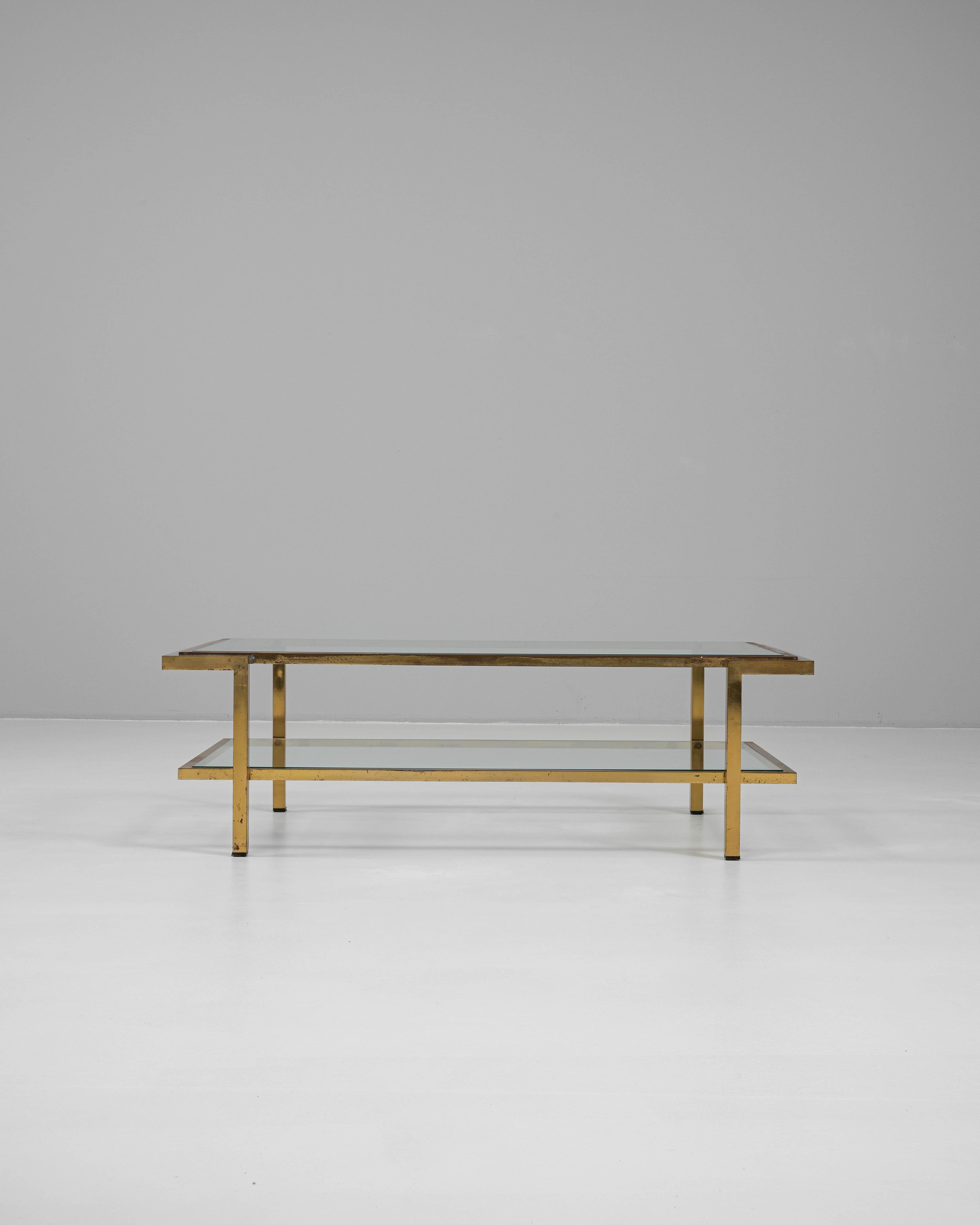 This 20th Century French coffee table features a sleek, rectilinear frame crafted from patinated brass, paired with two tiers of clear glass shelving for a refined, modernist look. The top and lower shelves are inset within the brass structure,