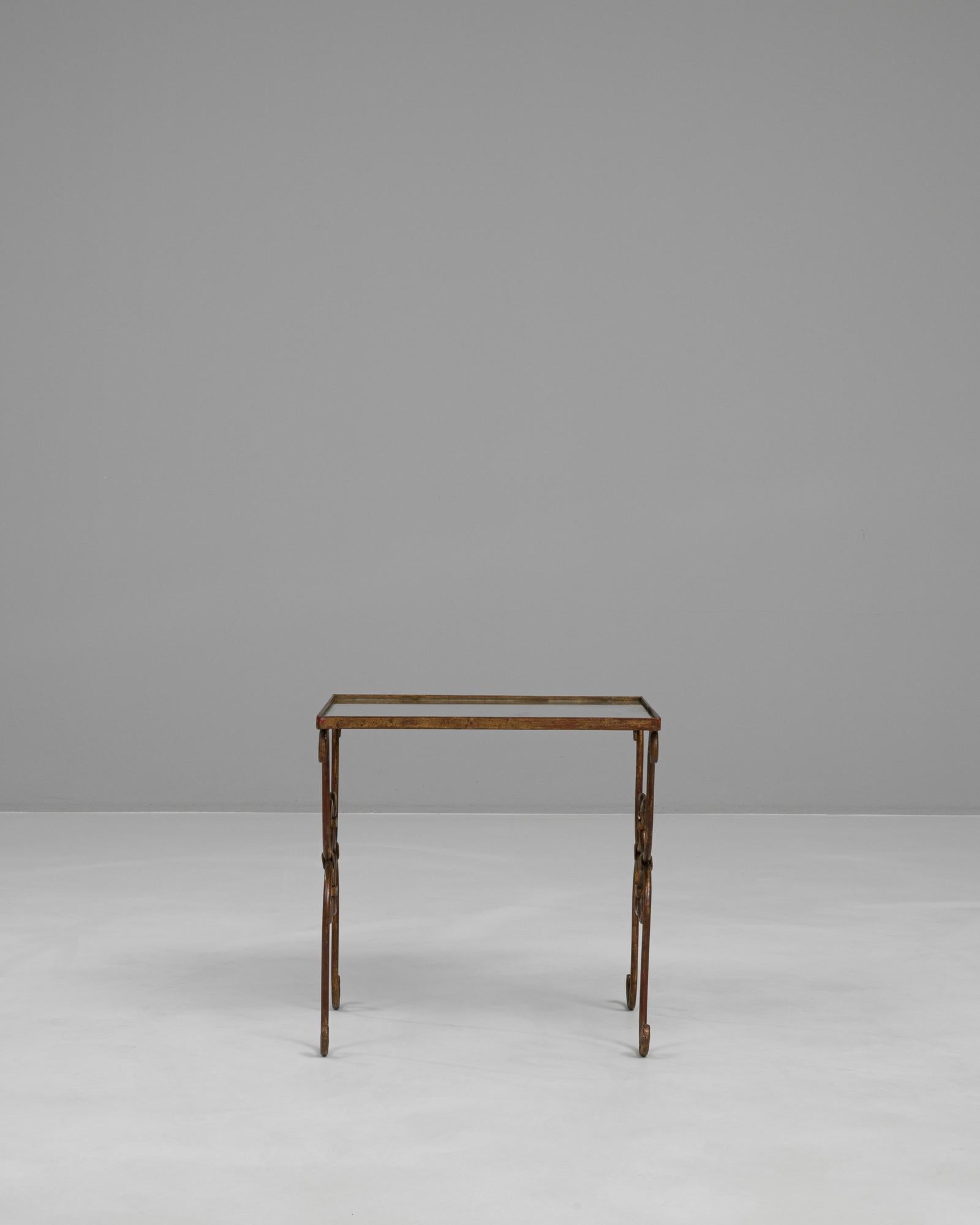 Cette table basse en laiton français du 20e siècle présente une silhouette élégante définie par sa base en laiton de style ferronnerie finement enroulée et sa patine chaude et naturellement vieillie. Le cadre présente des boucles décoratives