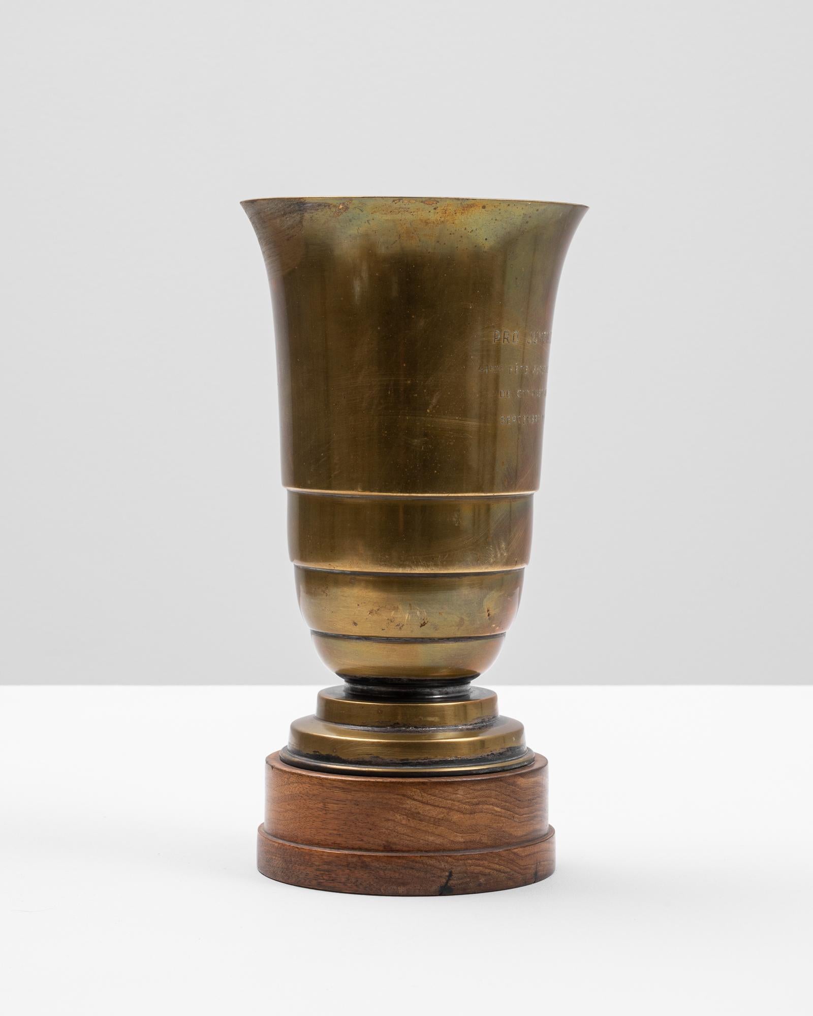 This 20th Century French brass cup stands as a striking decorative object with historical charm. Fashioned from solid brass, it features a flared lip, tiered bands, and a smooth, polished surface bearing light patina from age. The vessel rests on a