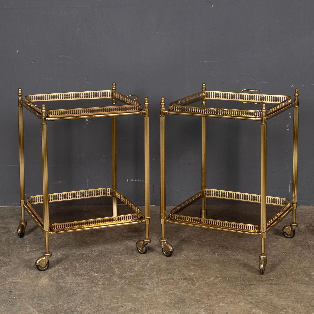 Two elegant drink trolleys crafted in France during the latter part of the 20th Century feature a beautifully fluted brass frame adorned with finials, providing sturdy support for two glass shelves. These exquisite pieces of furniture are not only