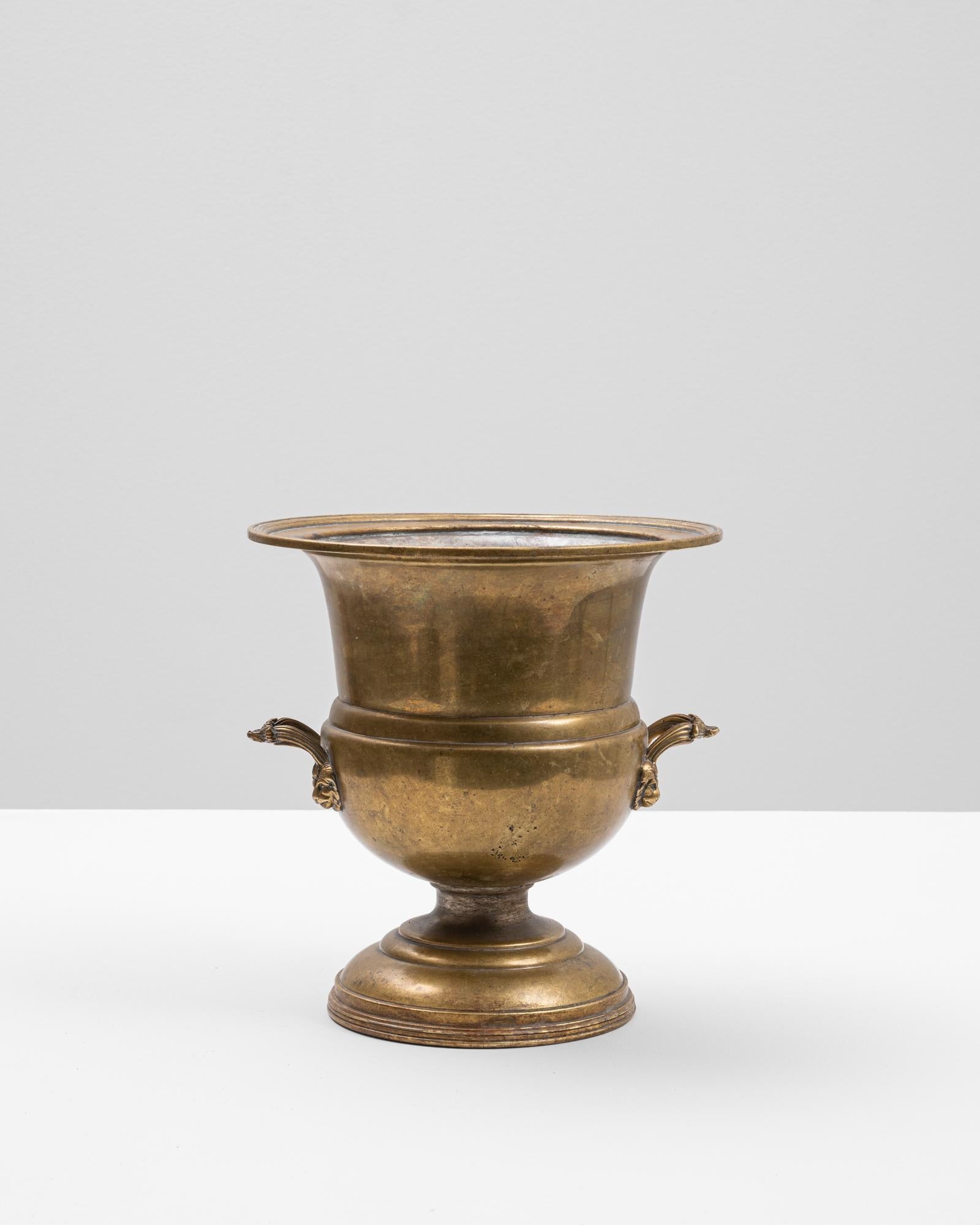 This 20th Century French brass ice bucket offers a stately silhouette and timeless appeal. Crafted from solid brass with a warm, naturally aged patina, the bucket features a classic urn form with a flared rim and rounded base. Twin handles shaped