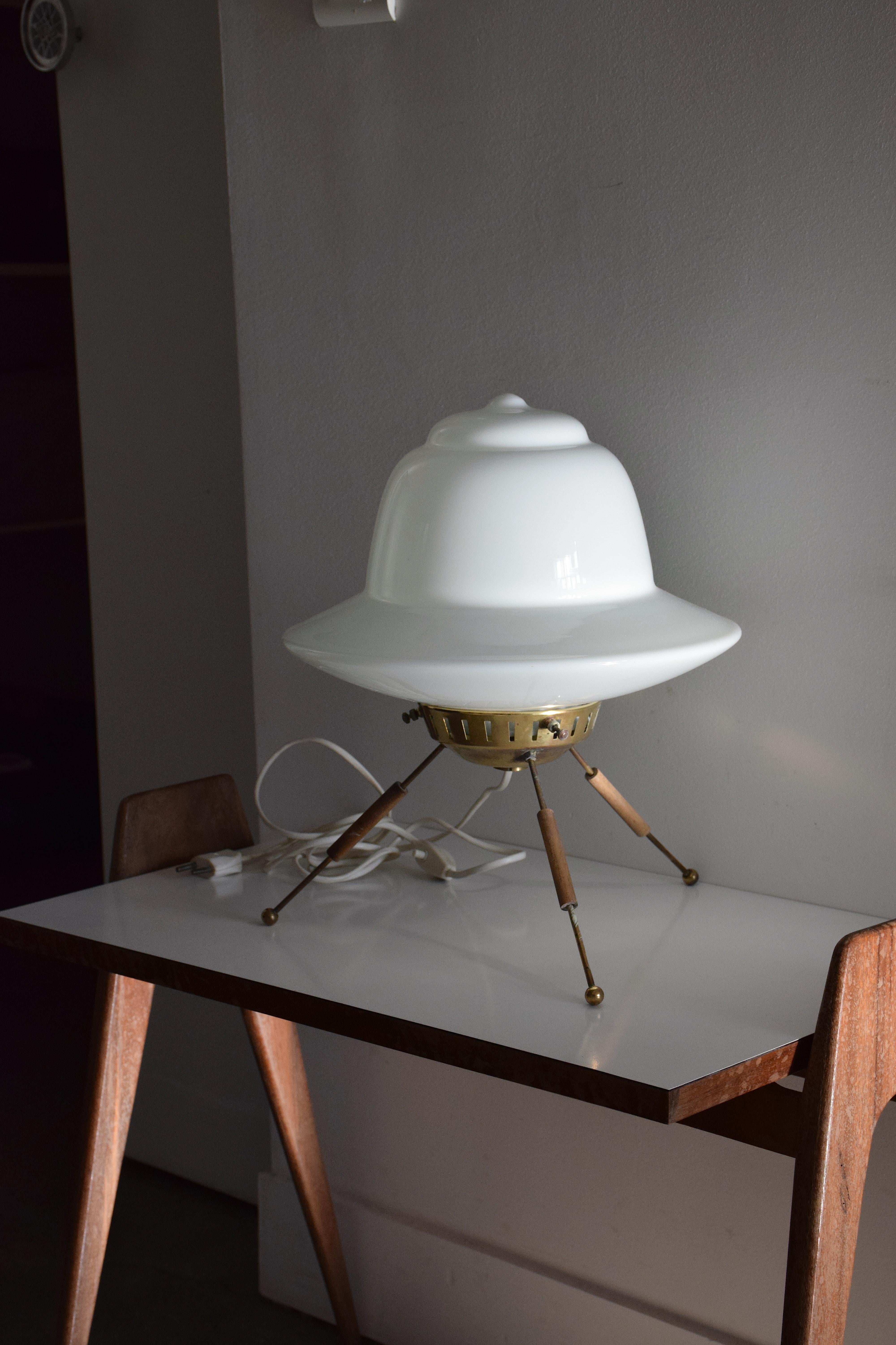 An astonishing Mid-Century Modern vintage table lamp in space-age style sitting on delicate brass and wooden splayed tripod legs. The shade is white opaline glass. A rare design that resembles a spaceship. Quite tall for its design. One of our