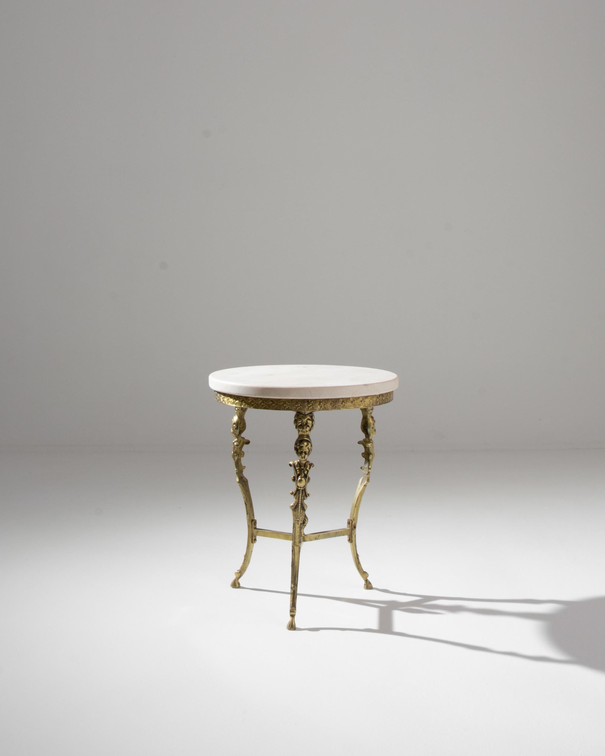 Ornate and light-footed, this vintage brass table conjures the elegance of an earlier age. Made in France in the 20th century, a circular tabletop of pale white marble sits atop a gilded base; dainty hoofed feet create a sprightly posture. The legs