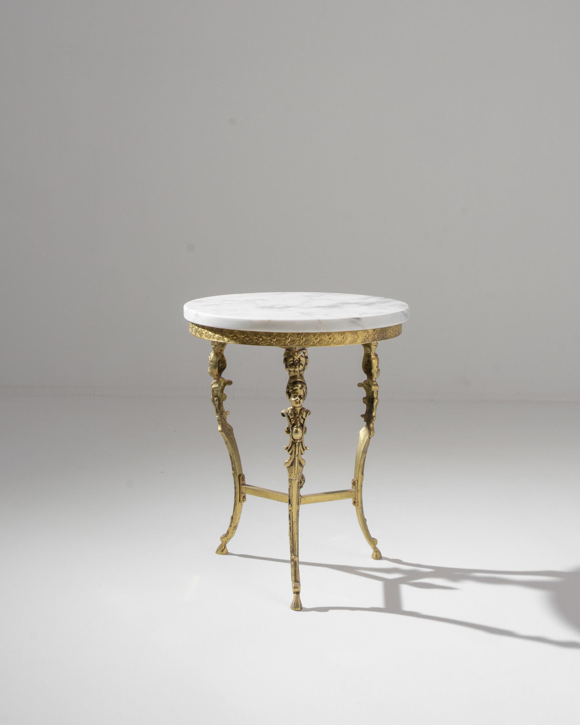 Ornate and light-footed, this vintage brass table conjures the elegance of an earlier age. Made in France in the 20th century, a circular tabletop of pale white marble sits atop a gilded base; dainty hoofed feet create a sprightly posture. The legs