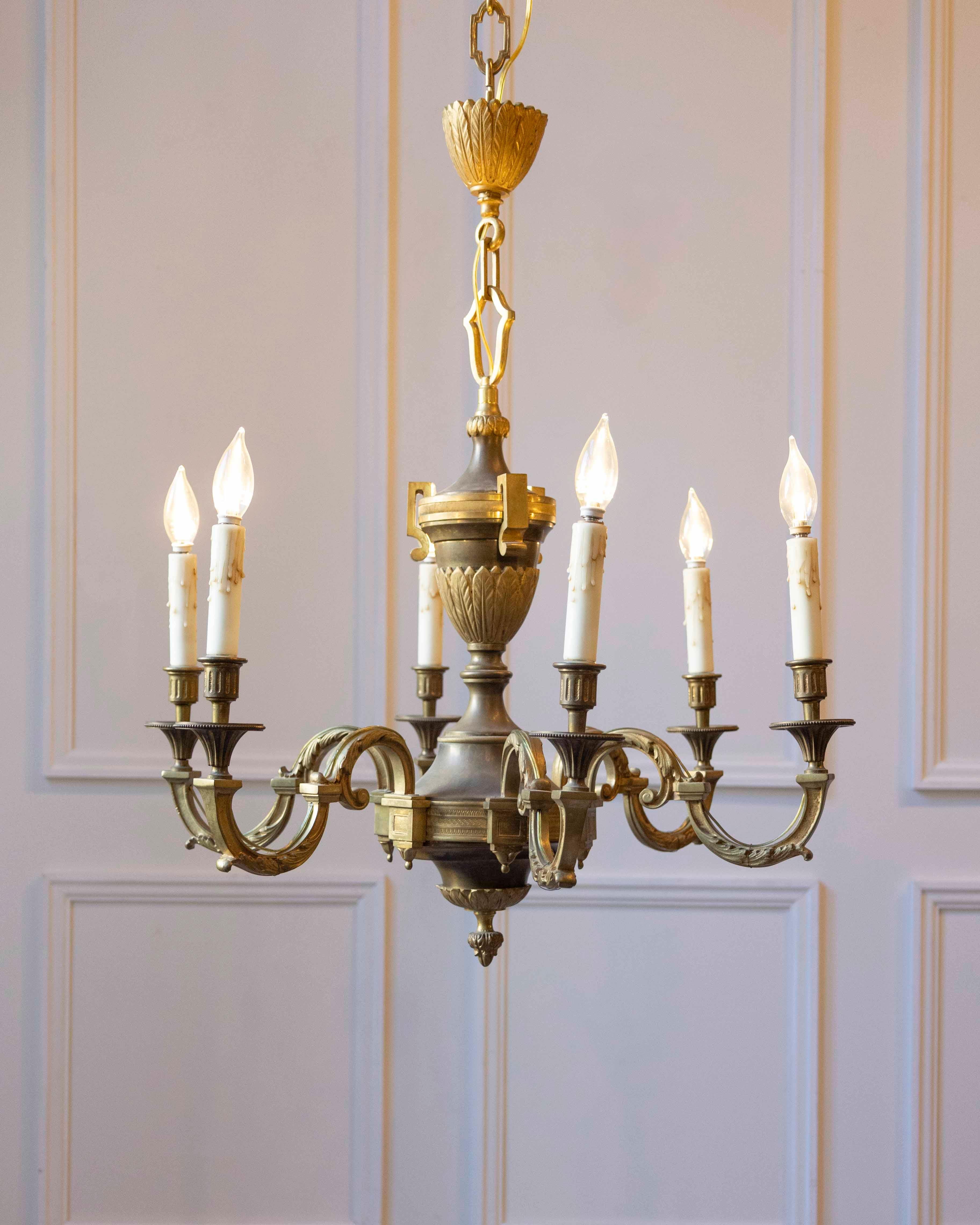 This 20th-century French bronze chandelier reflects a classical design vocabulary executed in solid cast bronze. The central column features tiered, urn-like forms and a fluted upper cup, all indicative of traditional French neoclassical lighting.