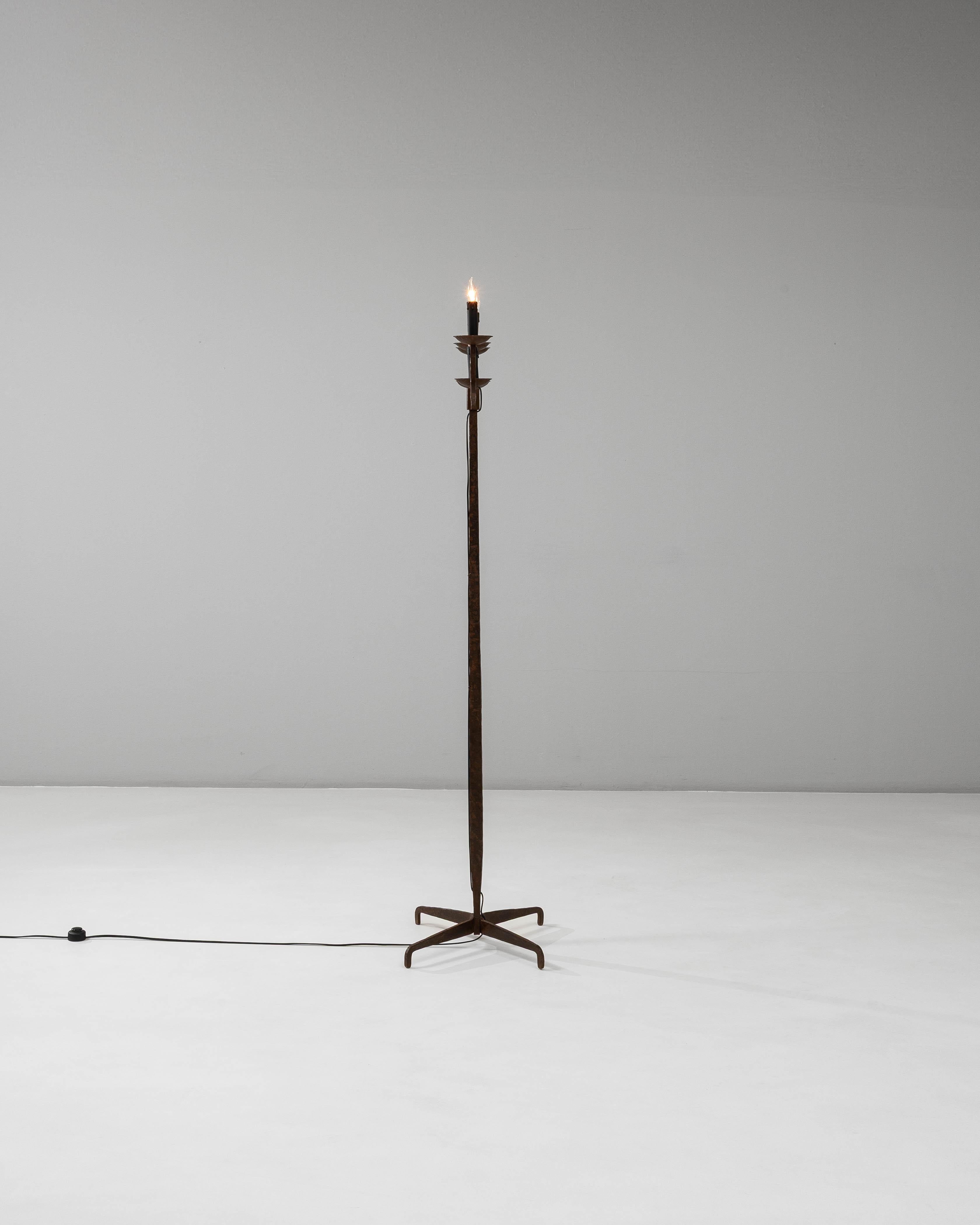 Una lampada a candelabro in ferro battuto francese del XX secolo, definita dalla sua materialità grezza e dalla sua sorprendente forma architettonica. L'alto stelo centrale forgiato si erge da una base angolare a quattro gambe, con ogni piede