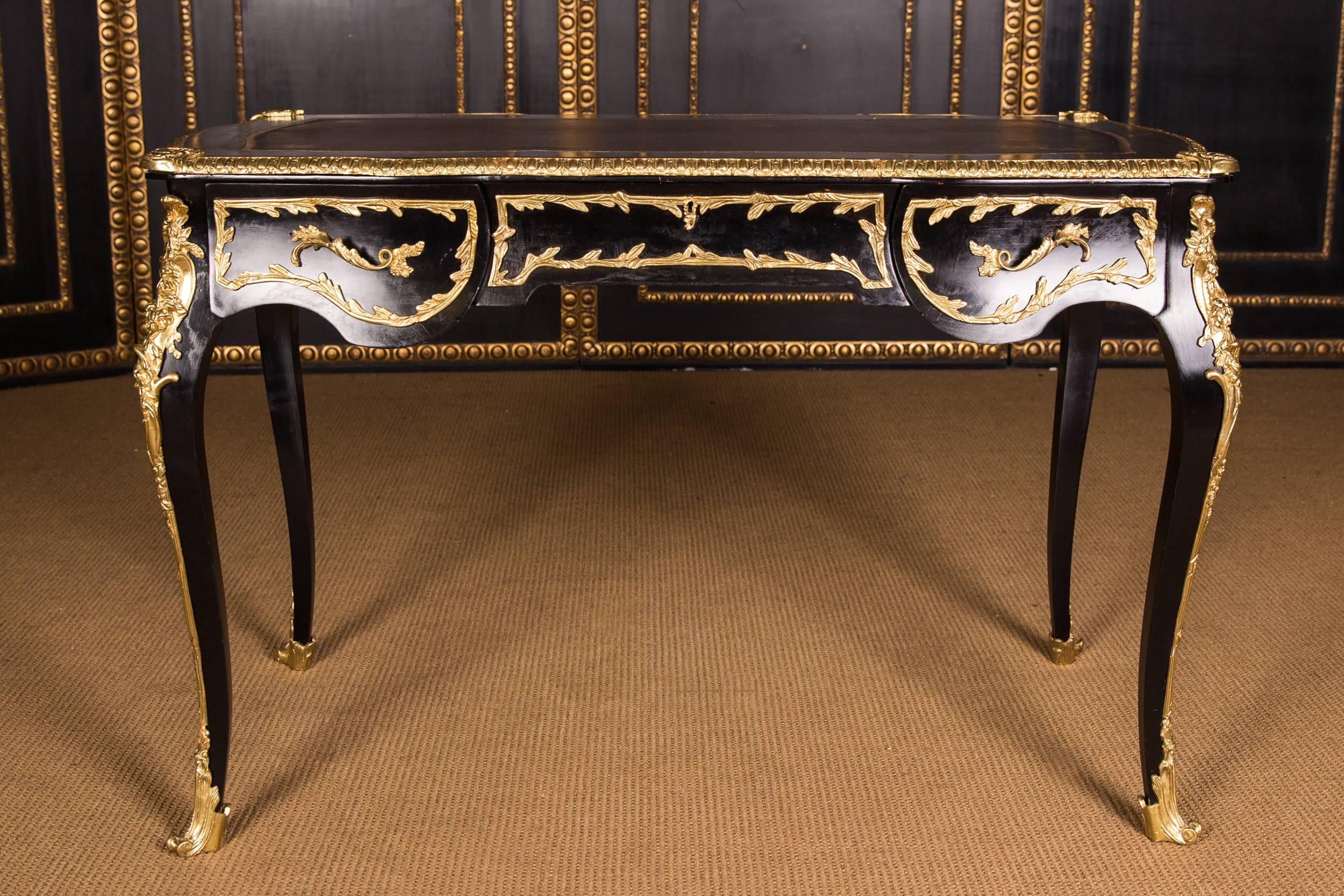 Black ebonized, four-sided passively curved frame base on high, elegantly curved squares. Encased in finely chiseled brass fittings. Slightly protruding tabletop with profiled decorated bronze lining and gold-imprinted leather imitation insert(the