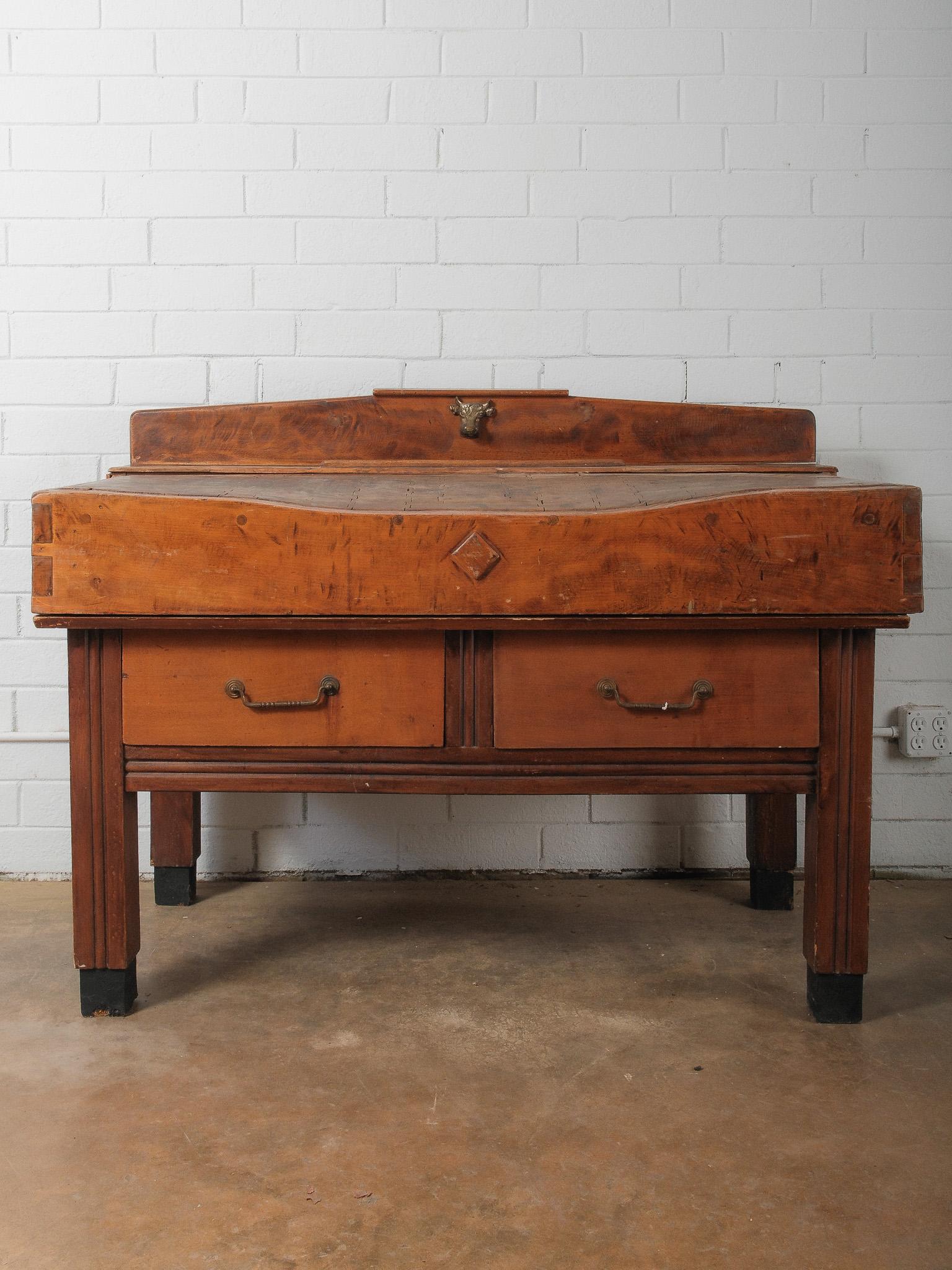 A remarkable early 20th-century French butcher’s block table, handcrafted in solid beechwood and retaining its rich, honeyed patina. This sculptural piece features a raised backsplash crowned with a decorative brass bull’s head mount—a classic