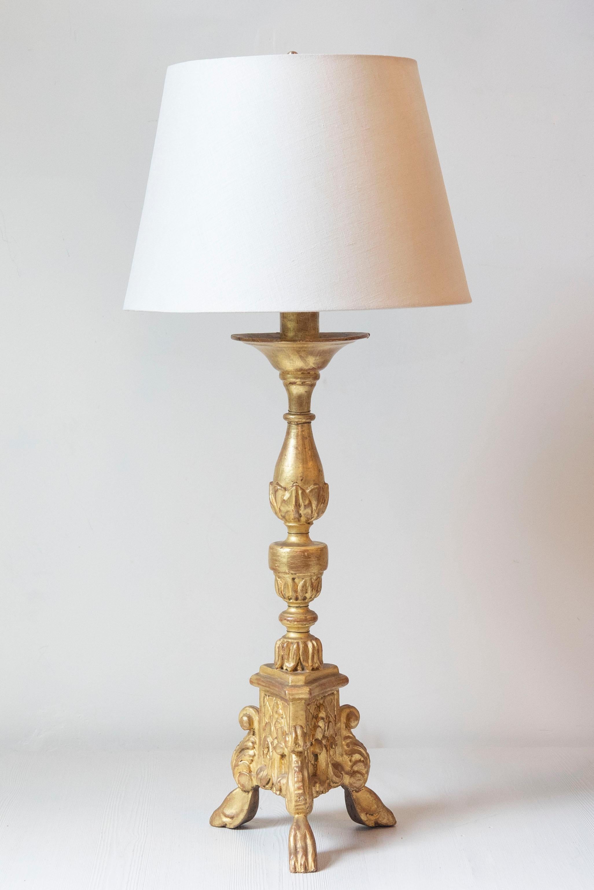 Cette exquise lampe de table française du XXe siècle est un exemple frappant de design classique associé à un riche savoir-faire artisanal. Fabriquée en bois sculpté et finie dans une dorure antique lustrée, la lampe présente une élégante colonne en