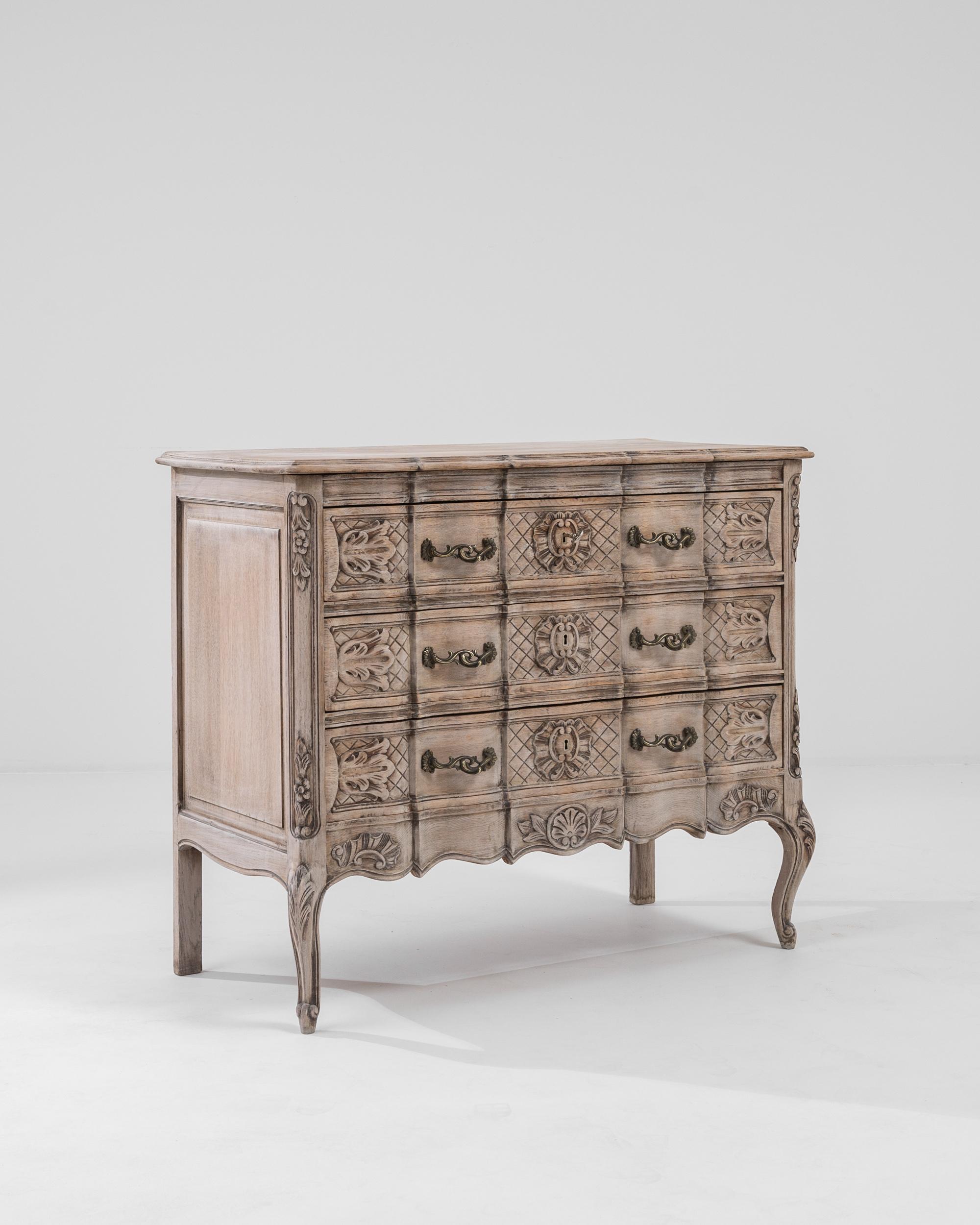 A 20th century carved oak commode produced in France, this opulent commode imparts a strong Louis XV influence with a soft touch. Standing on cabriole feet, the intricate commode features a scalloped apron, a beveled top and three large drawers